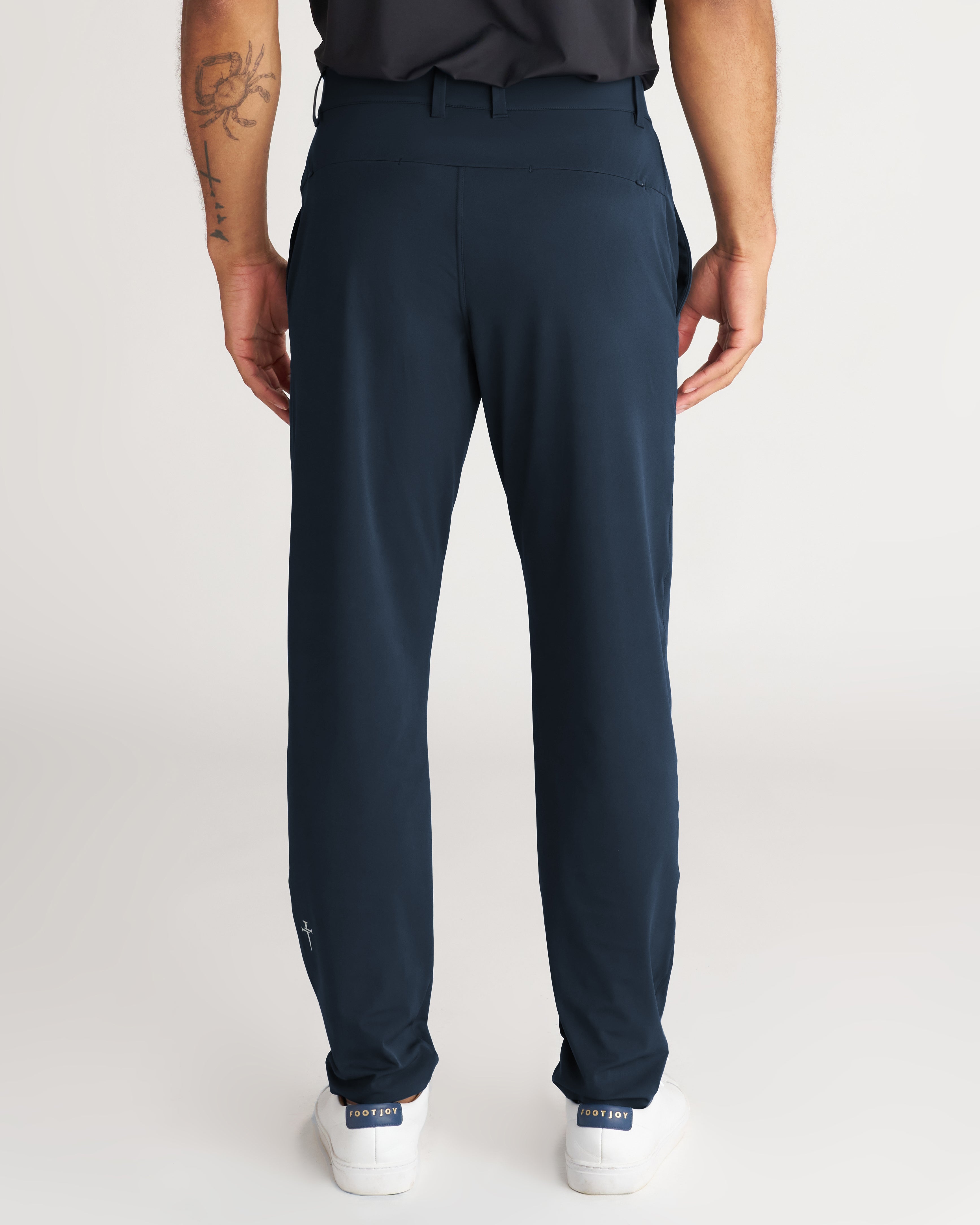 Back view of Links Golf Pant in Midnight Navy on a standing male model wearing white sneakers.