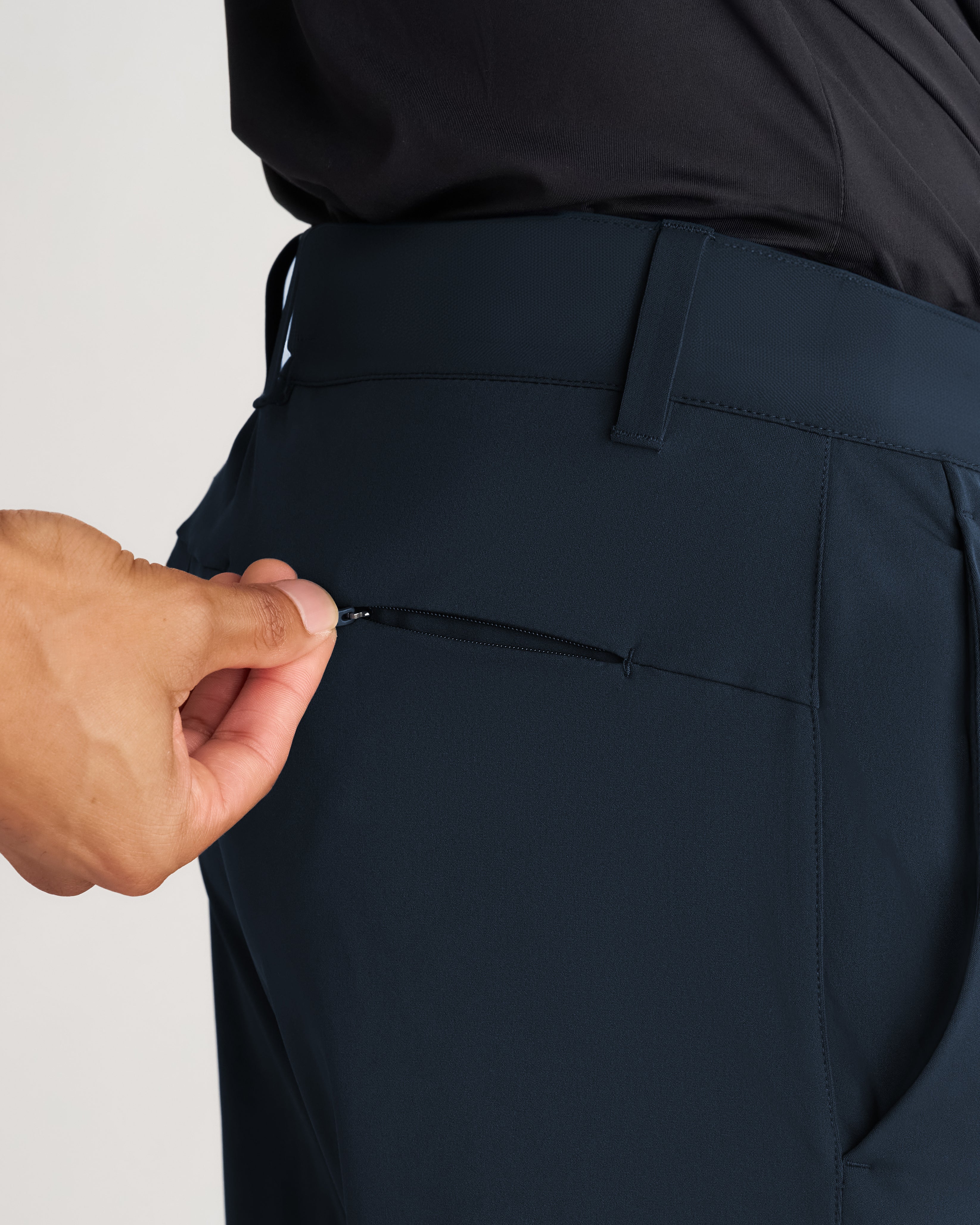 Close-up detail of Links Golf Pant in Midnight Navy showing a hand opening a rear zippered pocket.