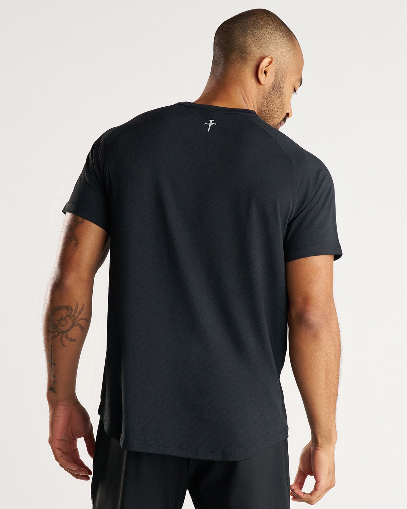 Back view of model wearing the Aion-Lite Tee Three Nails in black with small logo at nape.