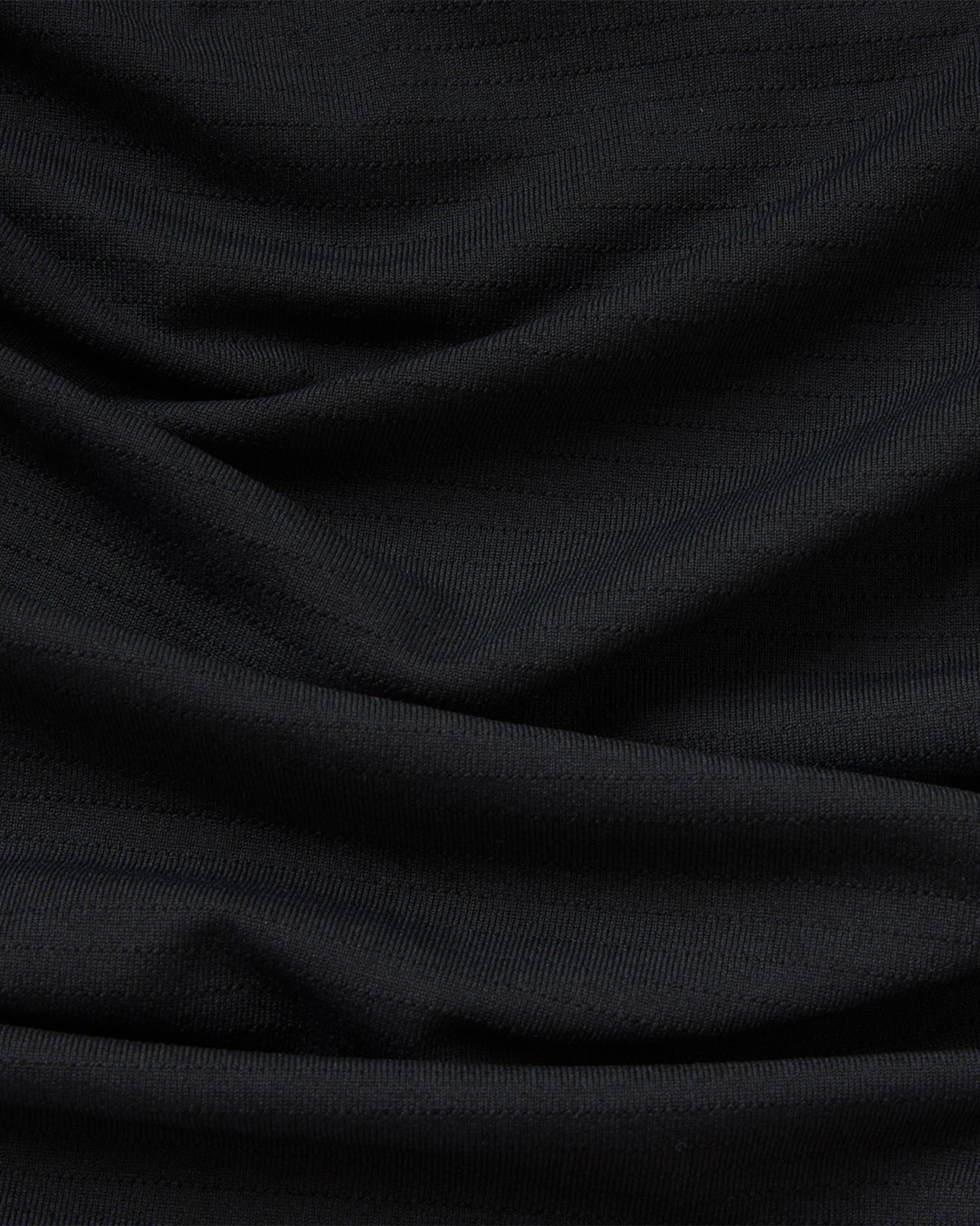 Close-up of the black Aion-Lite Tee Cross fabric texture showing soft draped folds and knit weave detail.