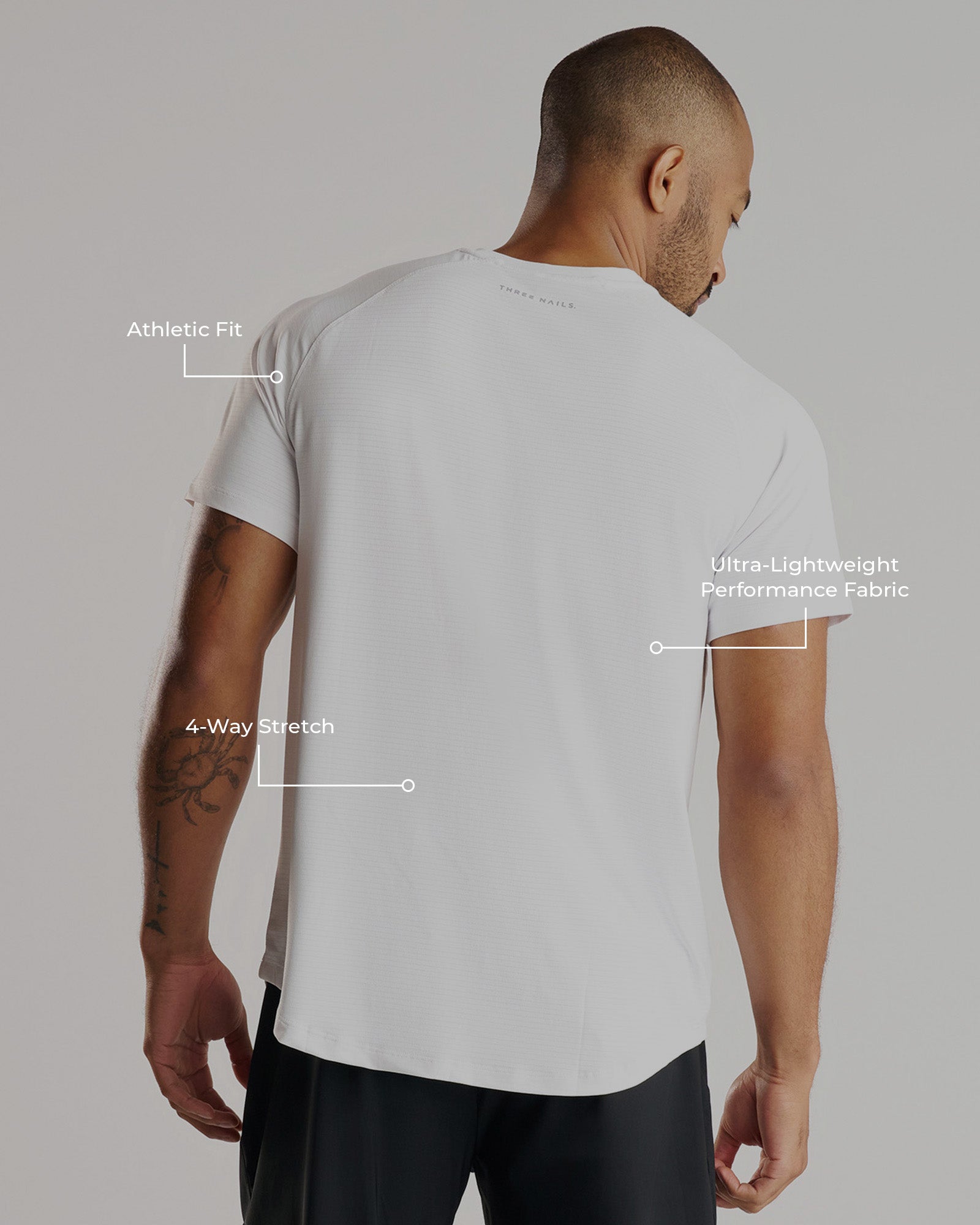 Back view of a man wearing the Aion-Lite Tee in white, with feature callouts highlighting fit, stretch, and fabric.