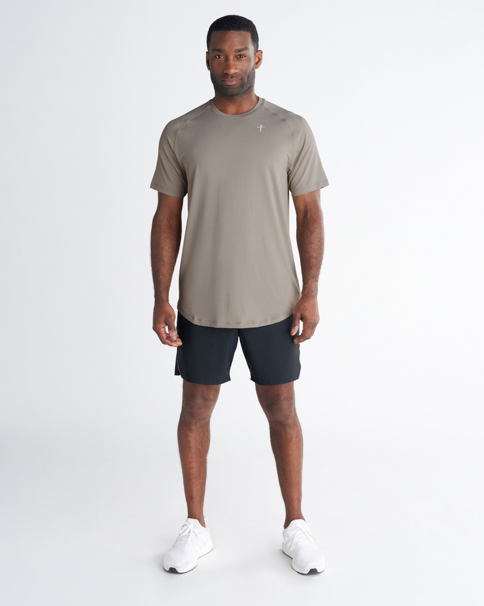 Man wearing the Core Tee in Sand, front view, paired with black shorts and white sneakers.