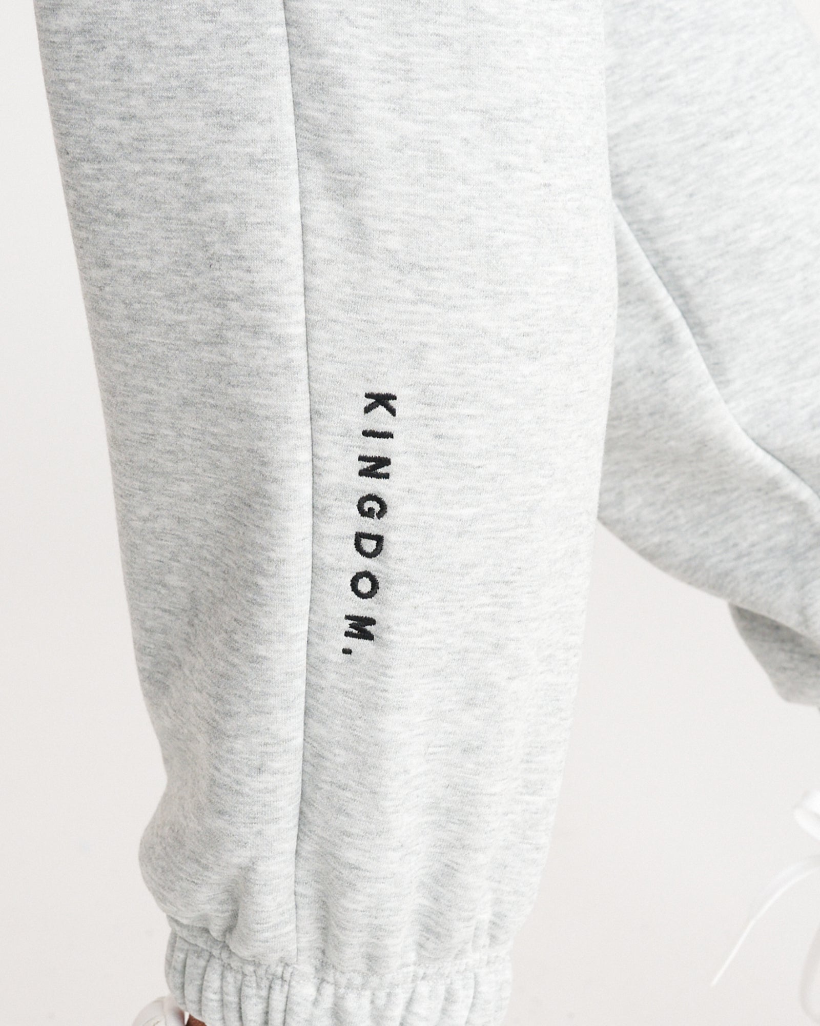 Close-up of Signature Fleece Sweatpants in Heather Grey showing embroidered KINGDOM. text on lower leg.