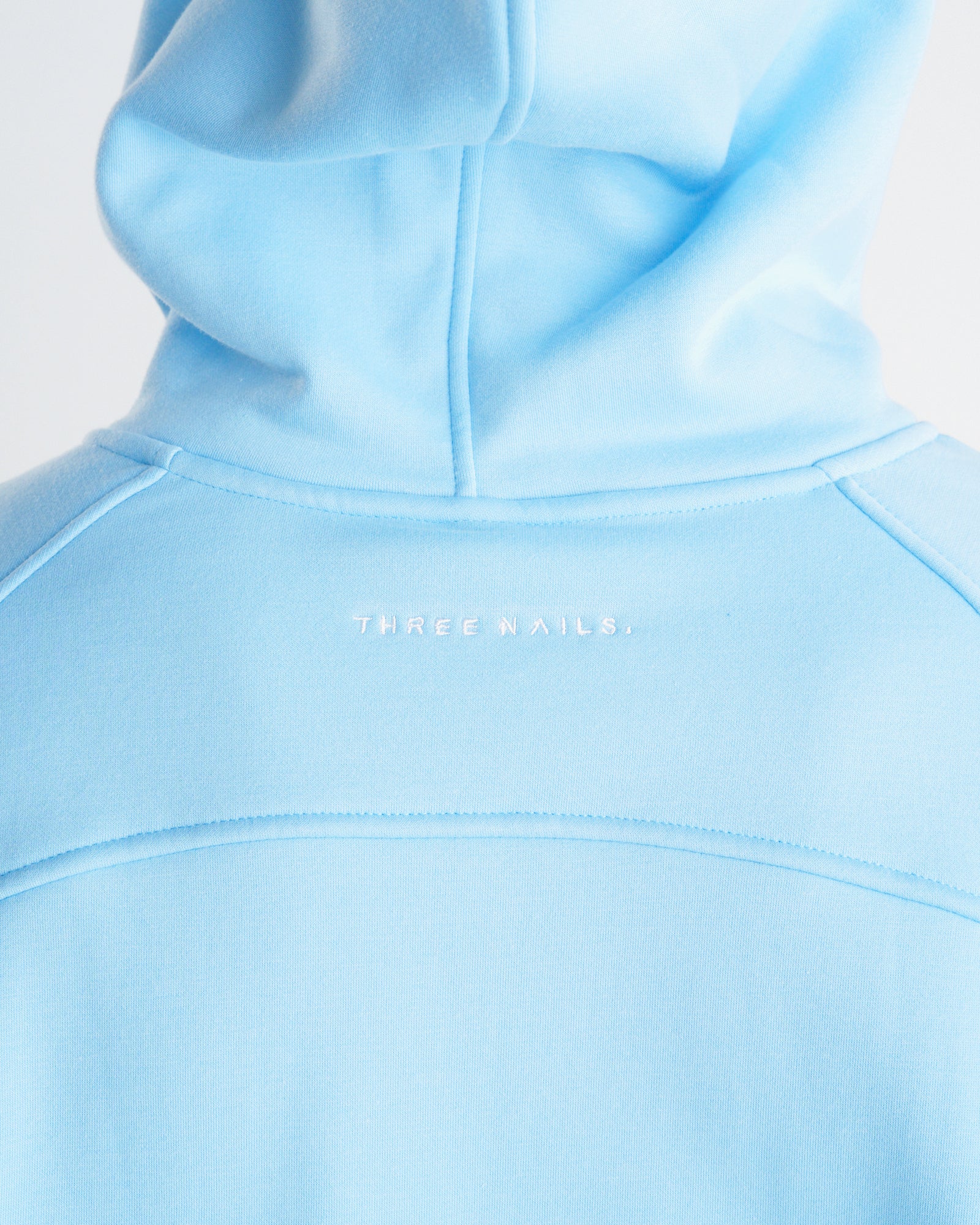 Close-up of the Sky Blue Signature Fleece Hoodie back neck area showing embroidered Three Nails branding.
