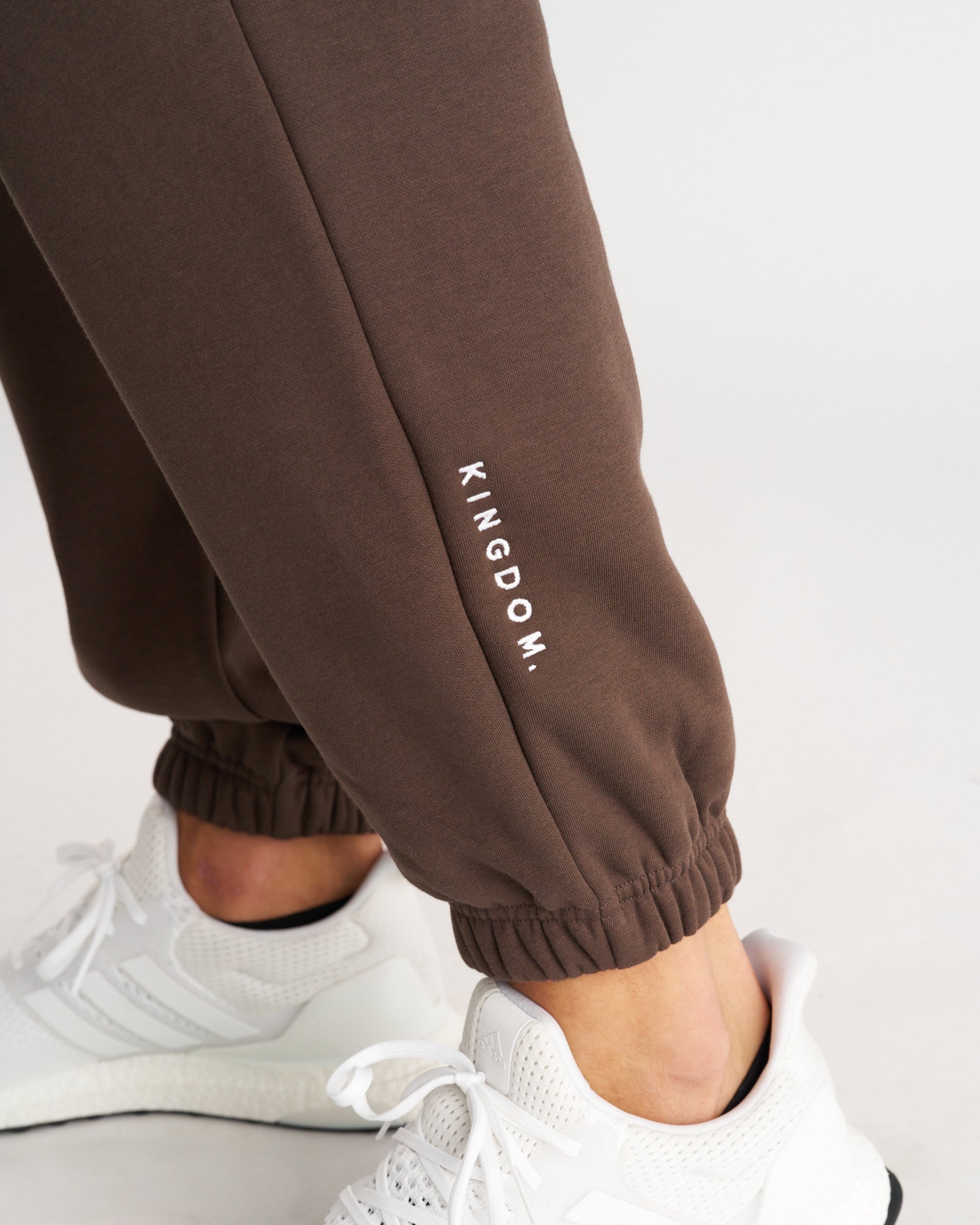 Close-up of Signature Fleece Sweatpants in Woodland Brown showing the cuffed ankle and KINGDOM. logo print.