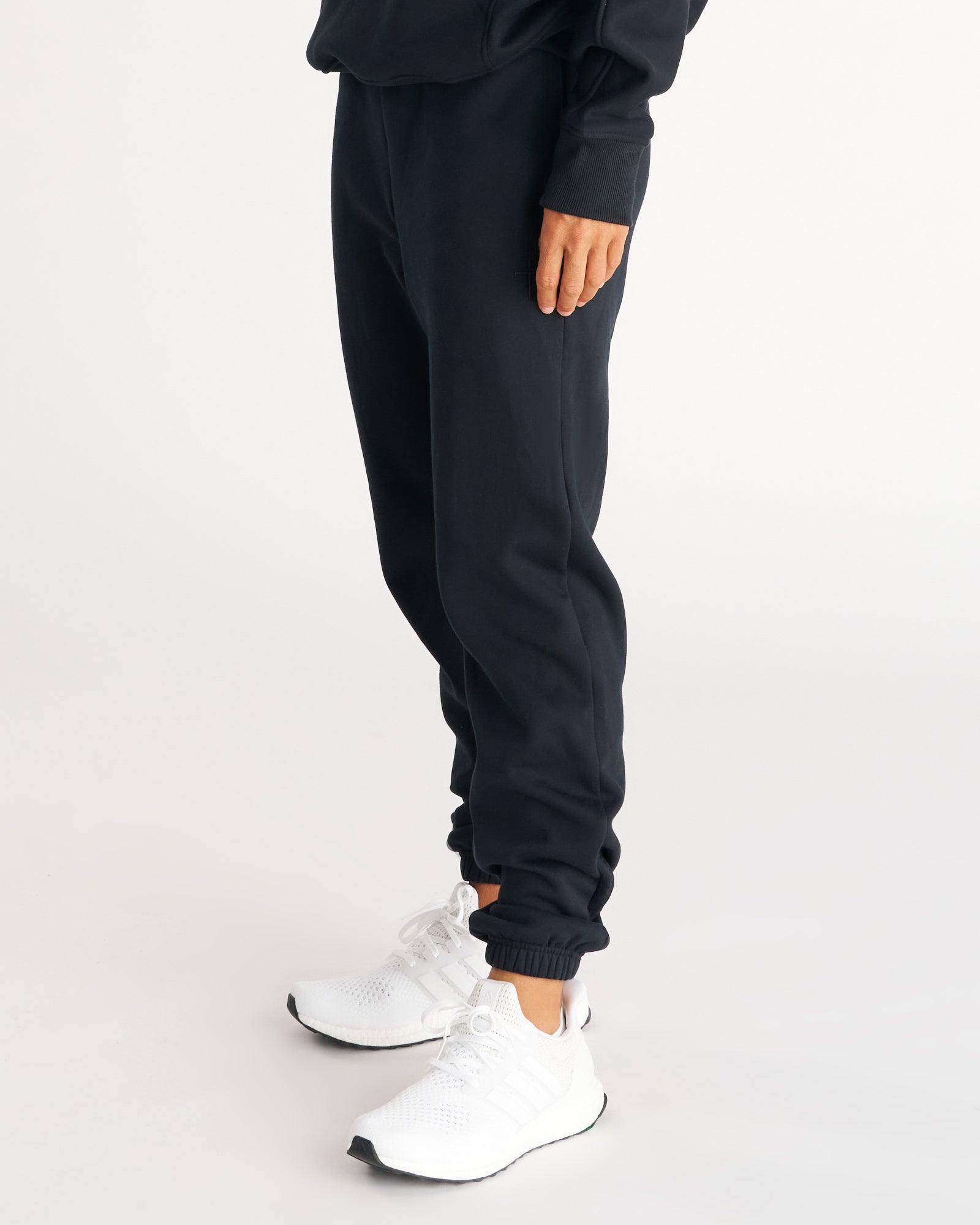 Signature Fleece Sweatpants in Blackout shown from a side angle on a model paired with white sneakers.