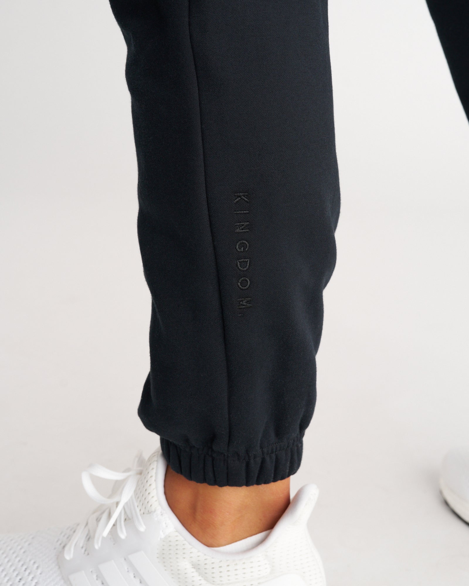 Close-up of Signature Fleece Sweatpants in Blackout showing tonal KINGDOM. embroidery on the lower leg cuff.
