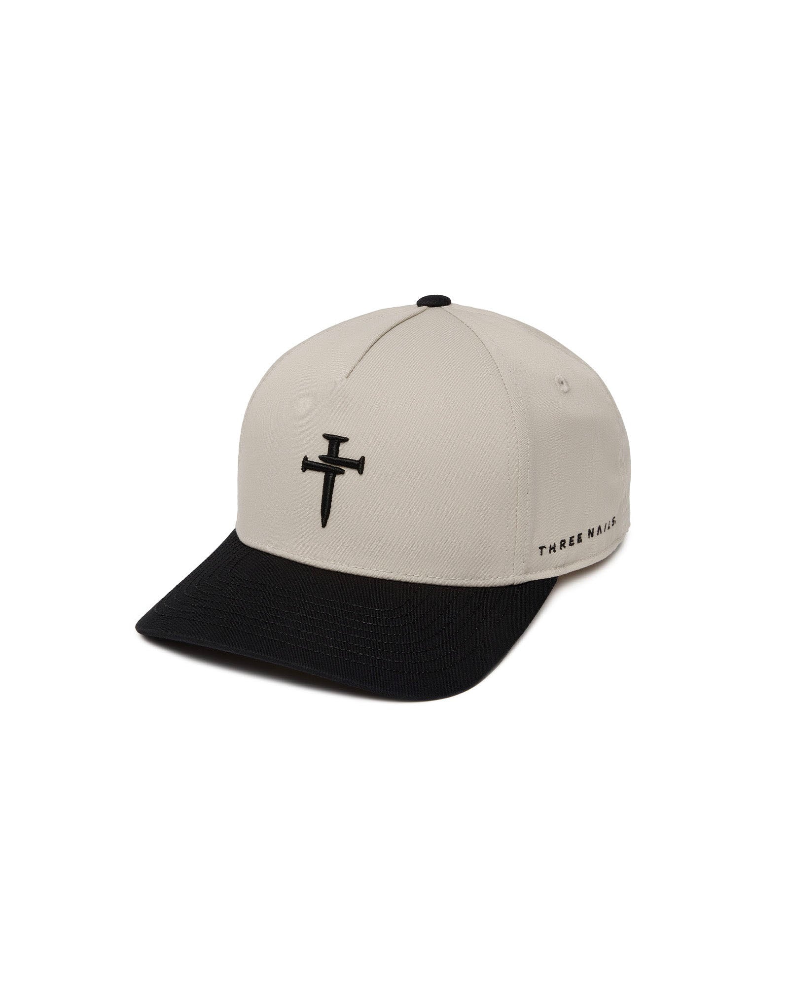 Signature Two-Tone Hat in cream and black with embroidered nail cross logo, flatlay on white background.