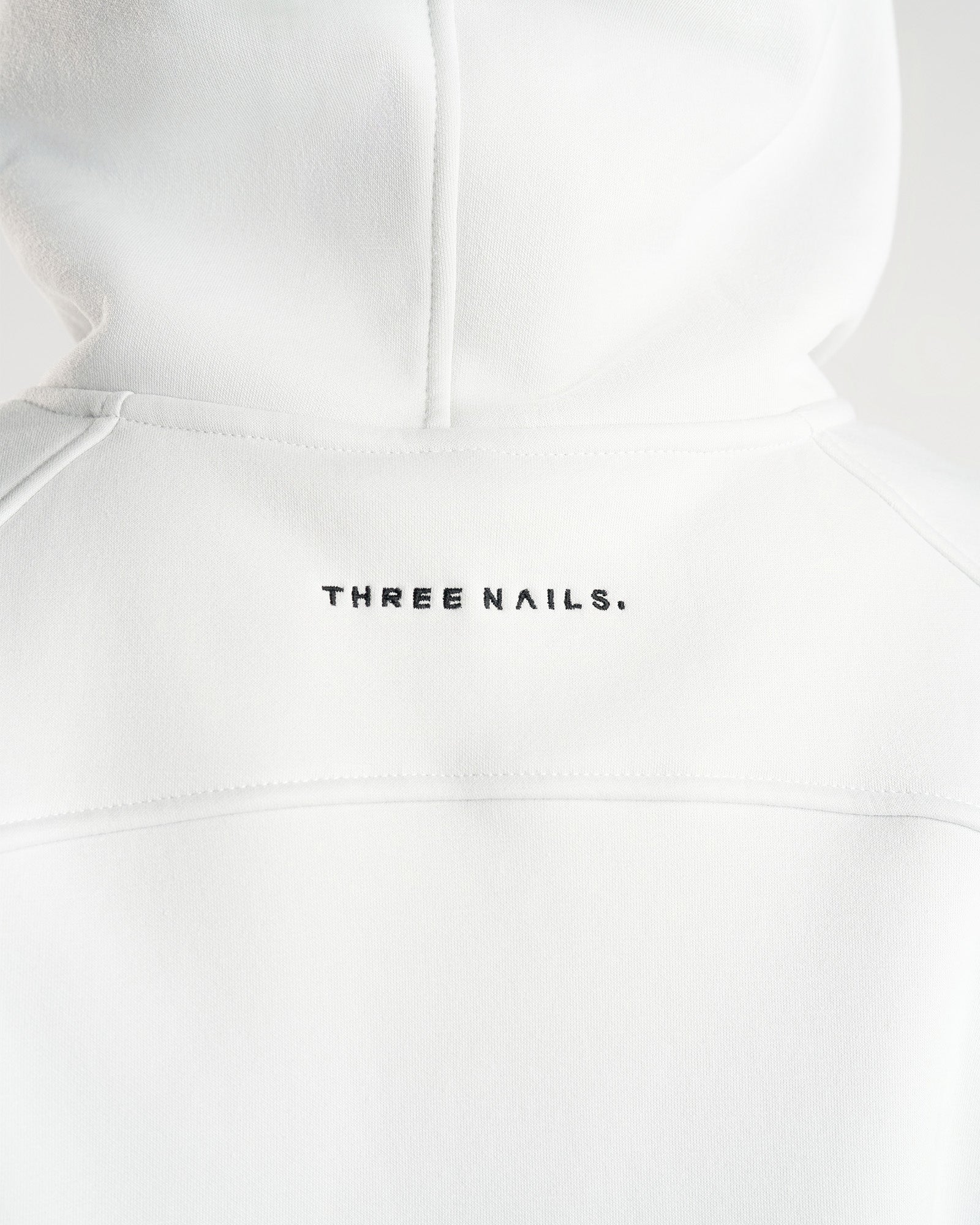 Close-up of the back neckline area of the Signature Fleece Hoodie in Stone showing embroidered Three Nails wordmark.