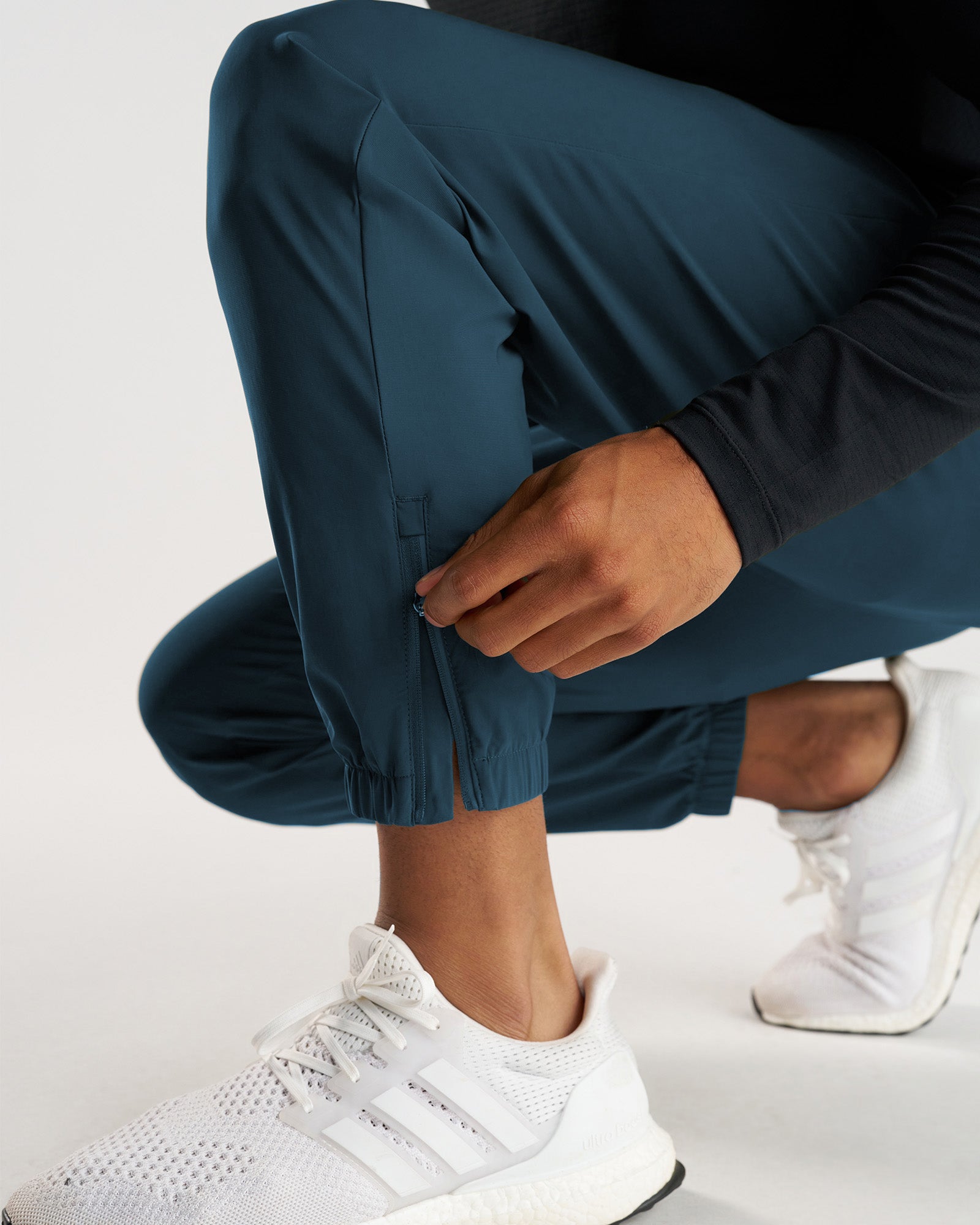 Close-up of Vapor-Lite Jogger in Midnight Navy showing elastic ankle cuff detail, model crouching in white Adidas sneakers.
