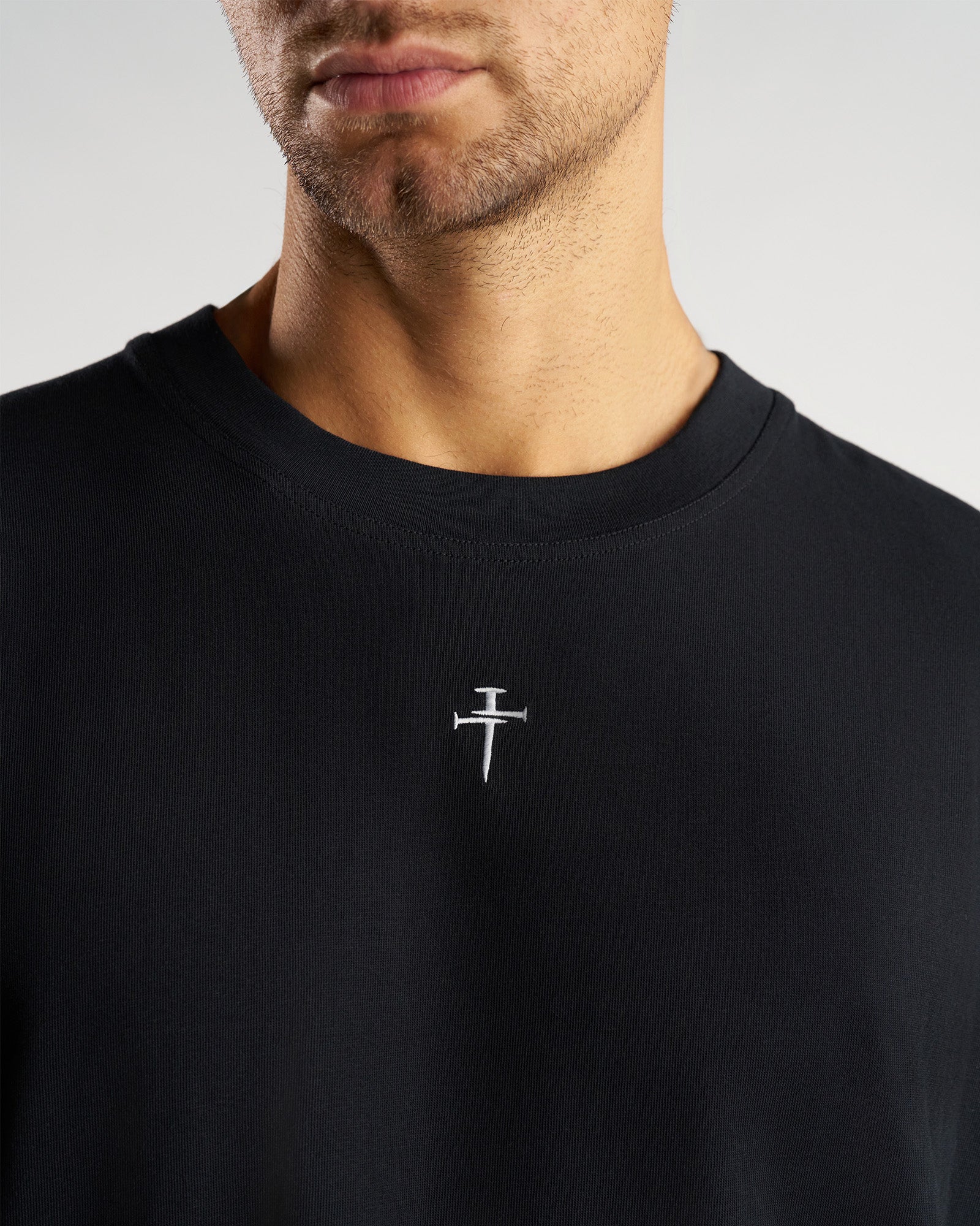 Close-up detail shot of the black Heavyweight Cotton Oversized Long Sleeve FHG showing the embroidered nail cross logo at center chest.