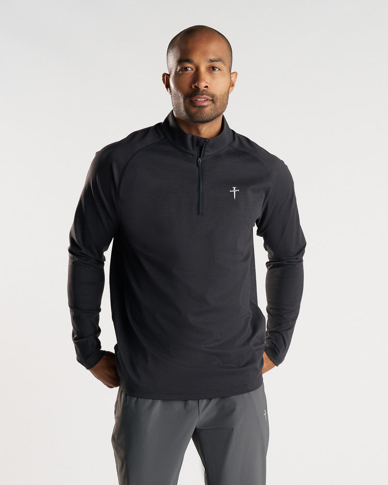 Man wearing black Core Quarter Zip front view, featuring a small cross logo and half-zip collar.