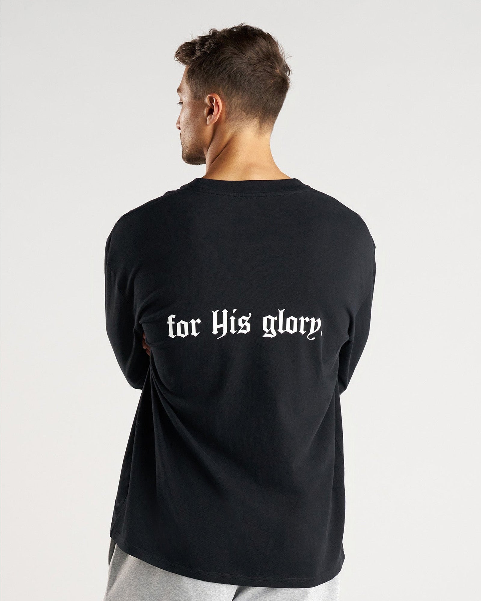 Back view of model wearing black FHG Heavyweight Cotton Oversized Long Sleeve with for His glory text on back.