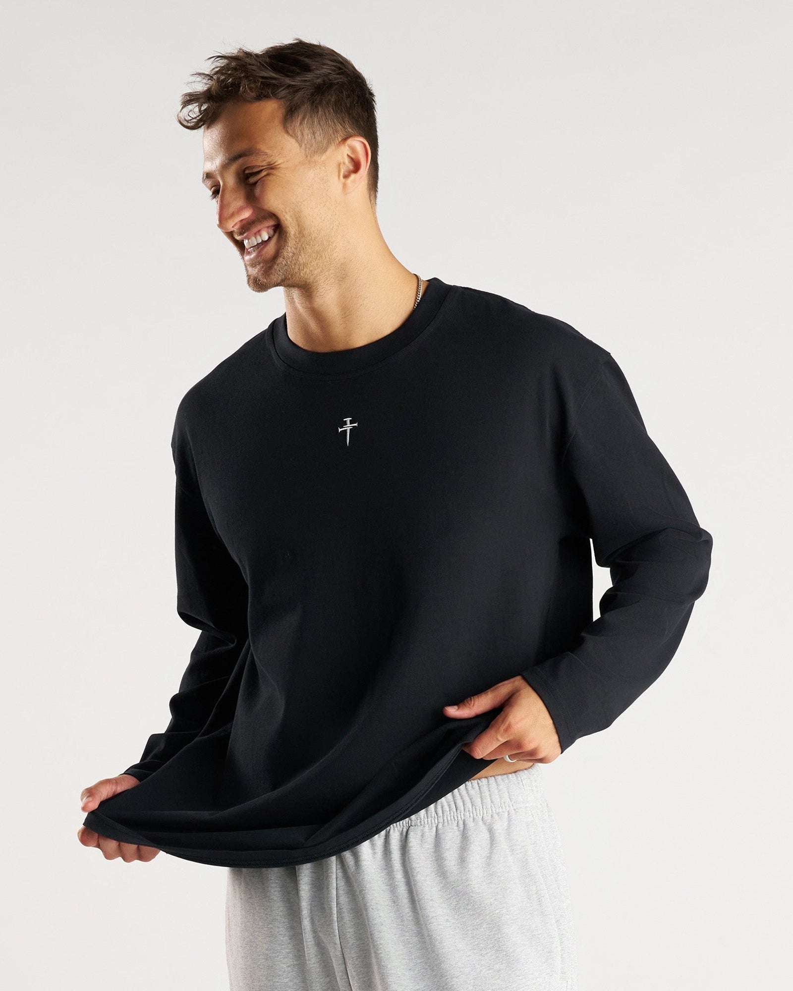 Man smiling, front view, wearing black FHG Heavyweight Cotton Oversized Long Sleeve with grey sweatpants.