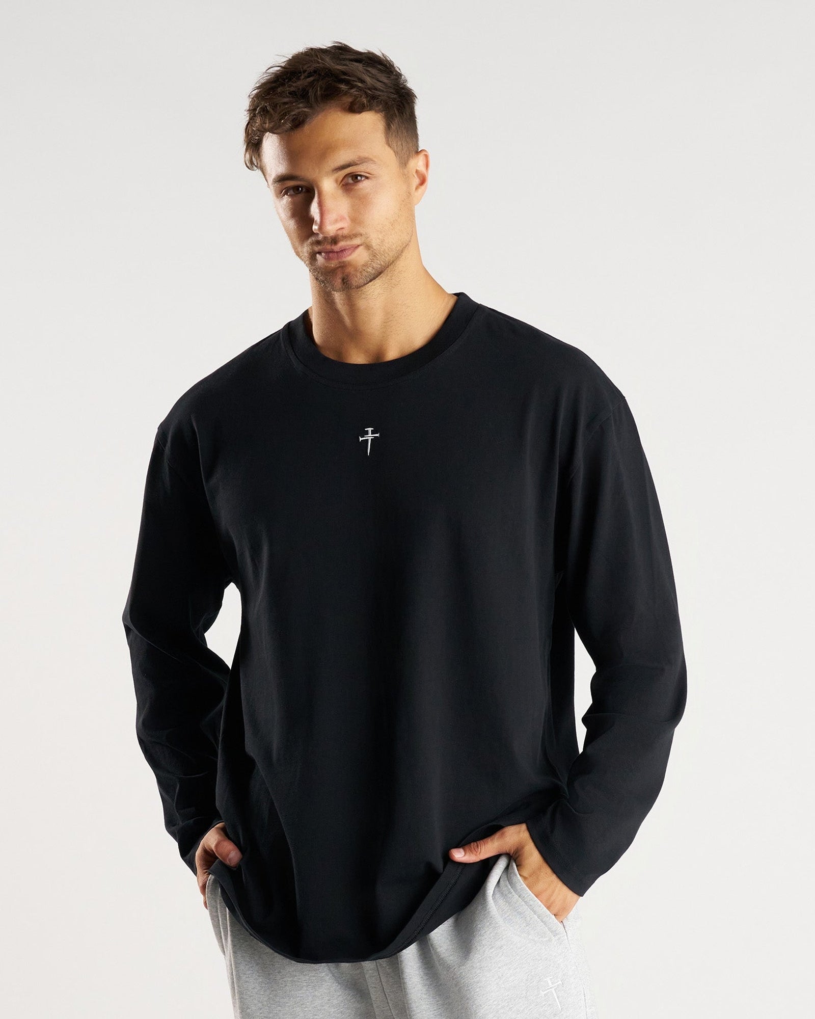 Man wearing black Heavyweight Cotton Oversized Long Sleeve FHG, front view, with small cross logo at chest.