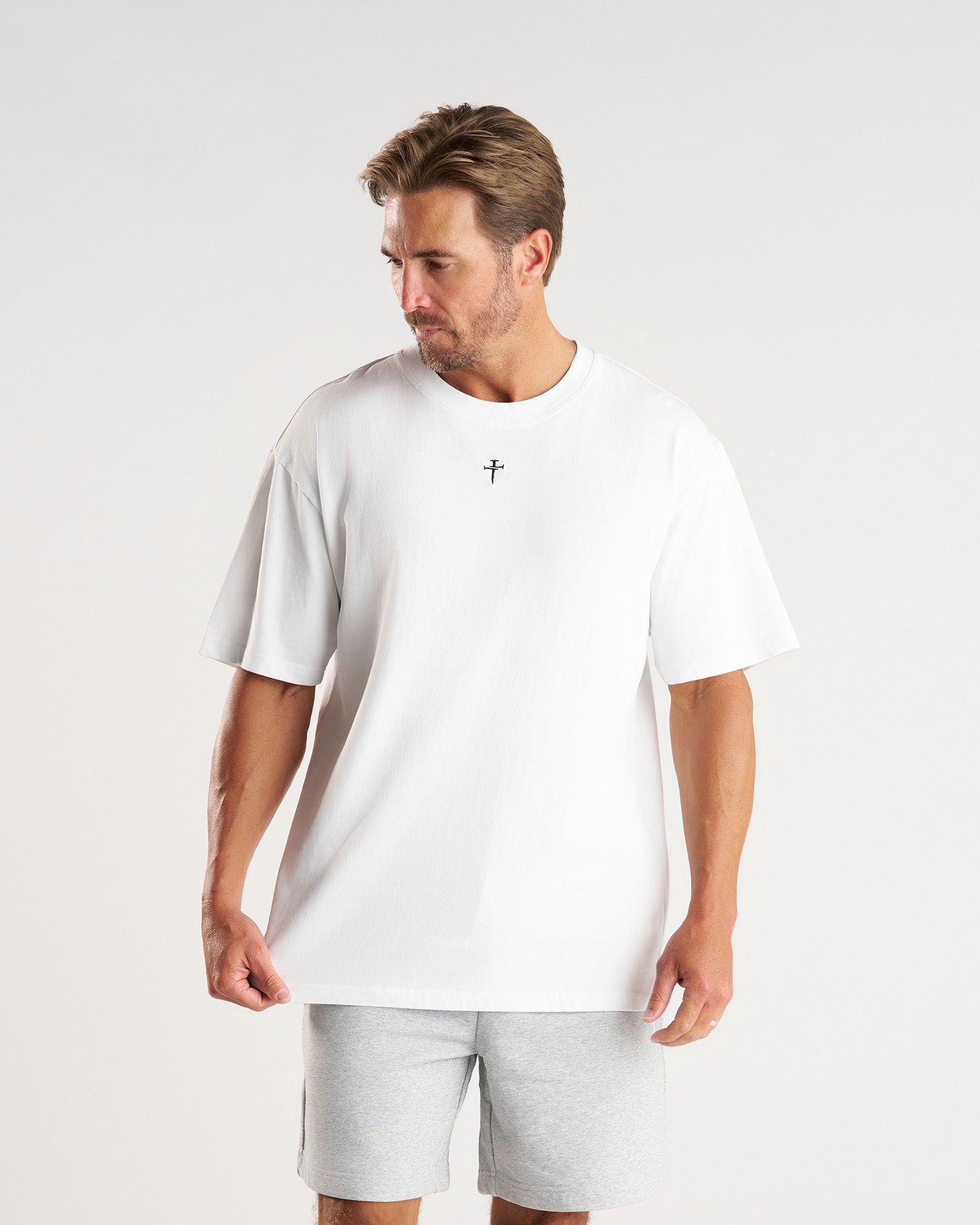 Man wearing white Heavyweight Cotton Oversized Tee FHG, front view, with small cross logo at chest.