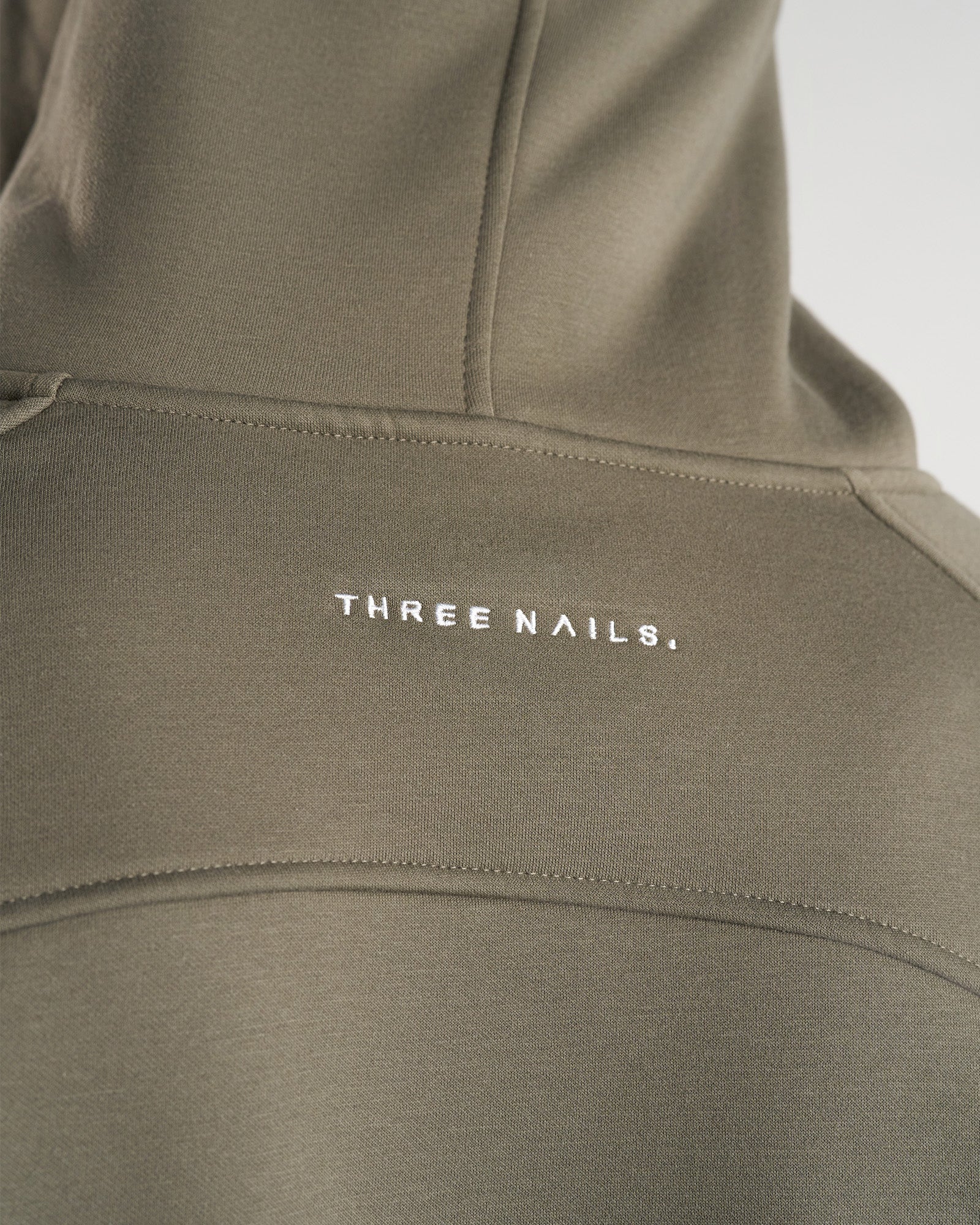 Close-up of the upper back detail on the Signature Fleece Hoodie in Sage, showing the Three Nails logo embroidery.