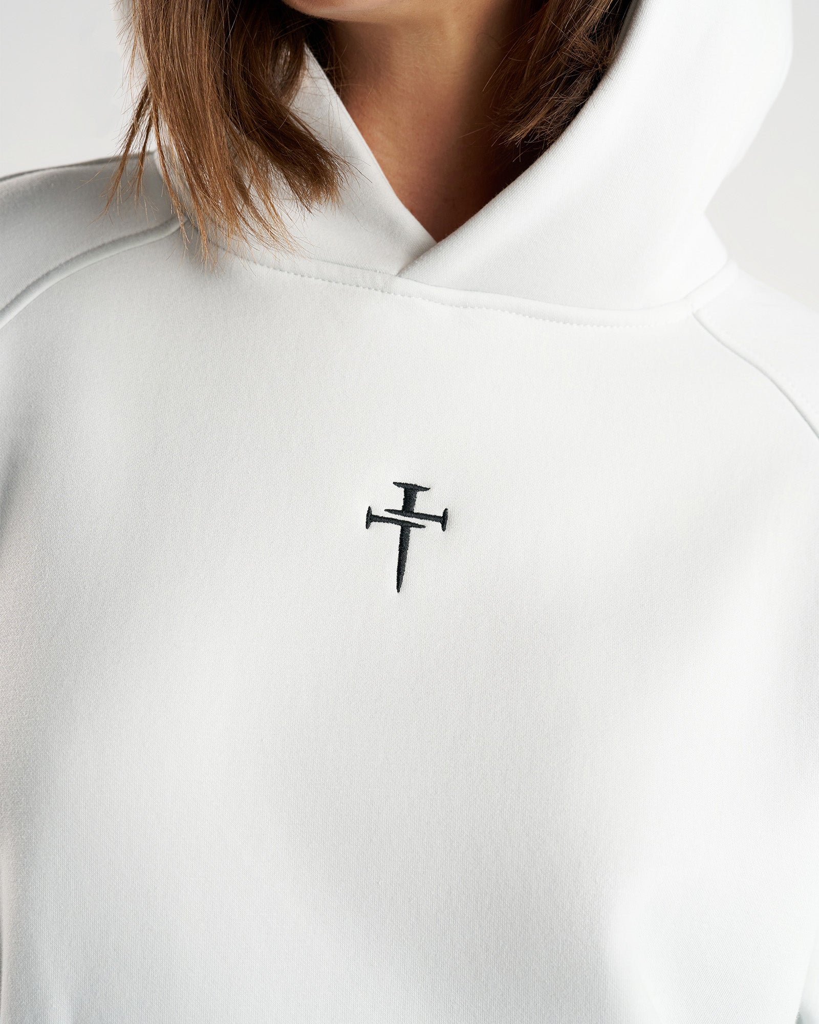 Close-up of the Signature Fleece Hoodie in Stone showing embroidered nails cross logo on chest.