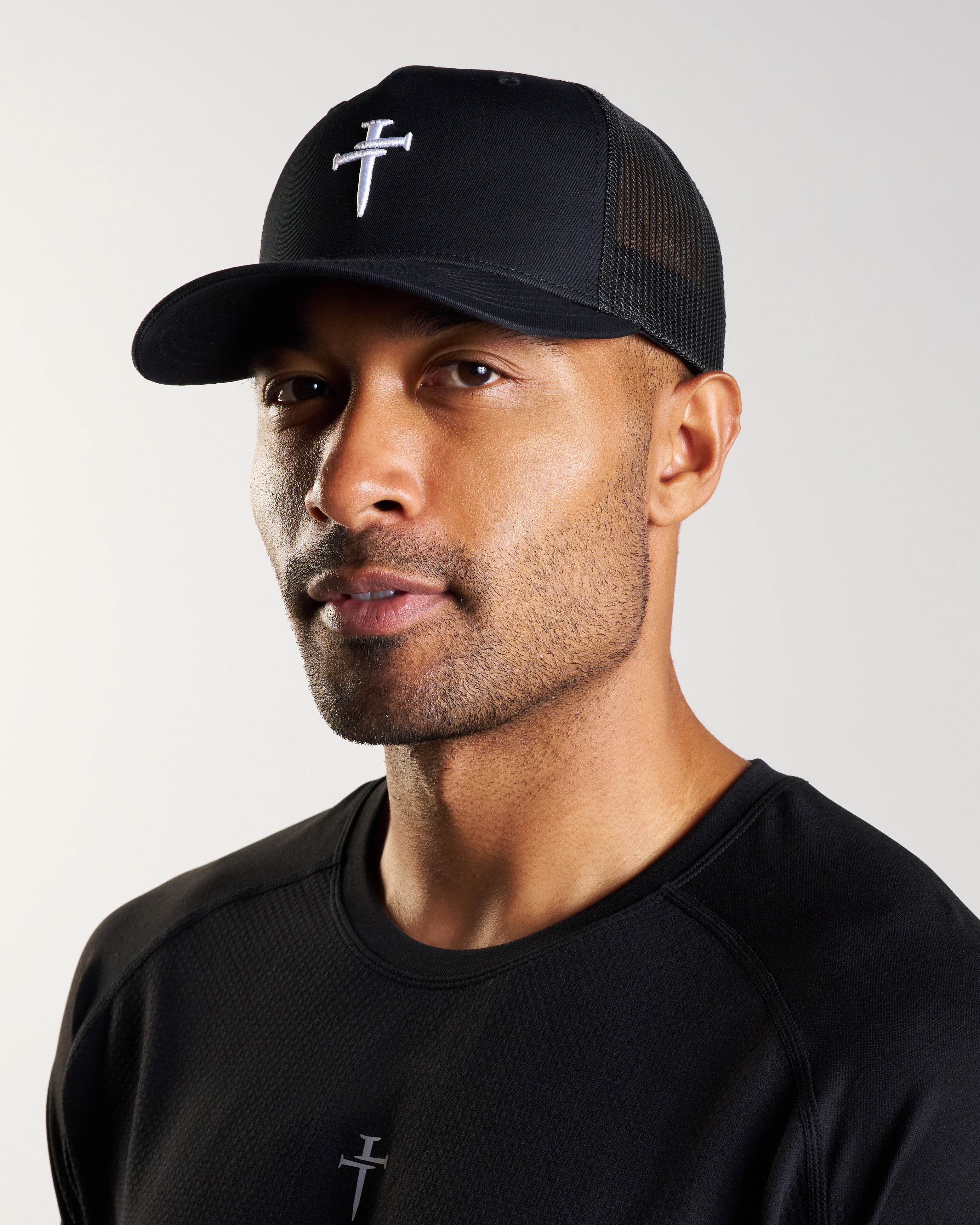 Male model wearing black Signature Trucker Hat, three-quarter angle, with matching black athletic shirt.