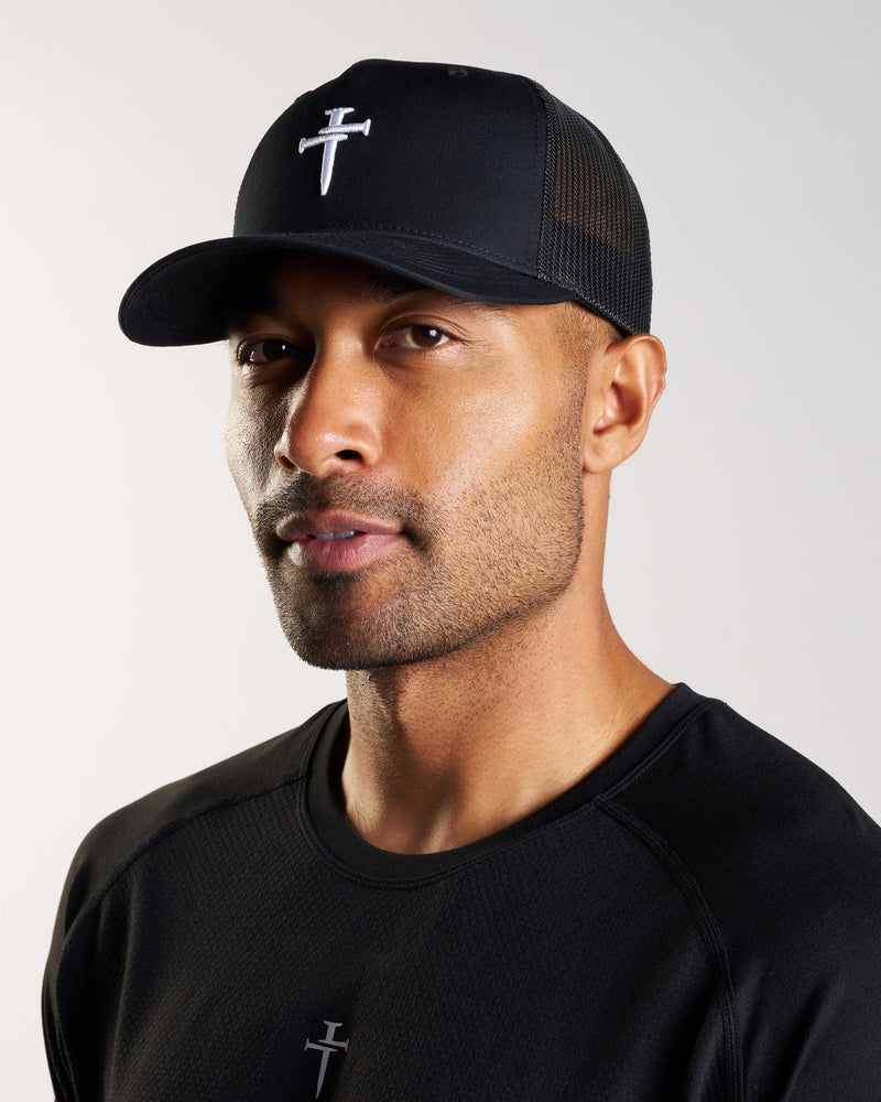 Male model wearing black Signature Trucker Hat, three-quarter angle, with matching black athletic shirt.