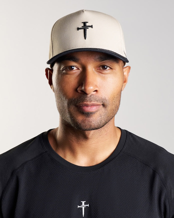 Man wearing Signature Two-Tone Hat in tan and black, front view, featuring embroidered nail cross logo.