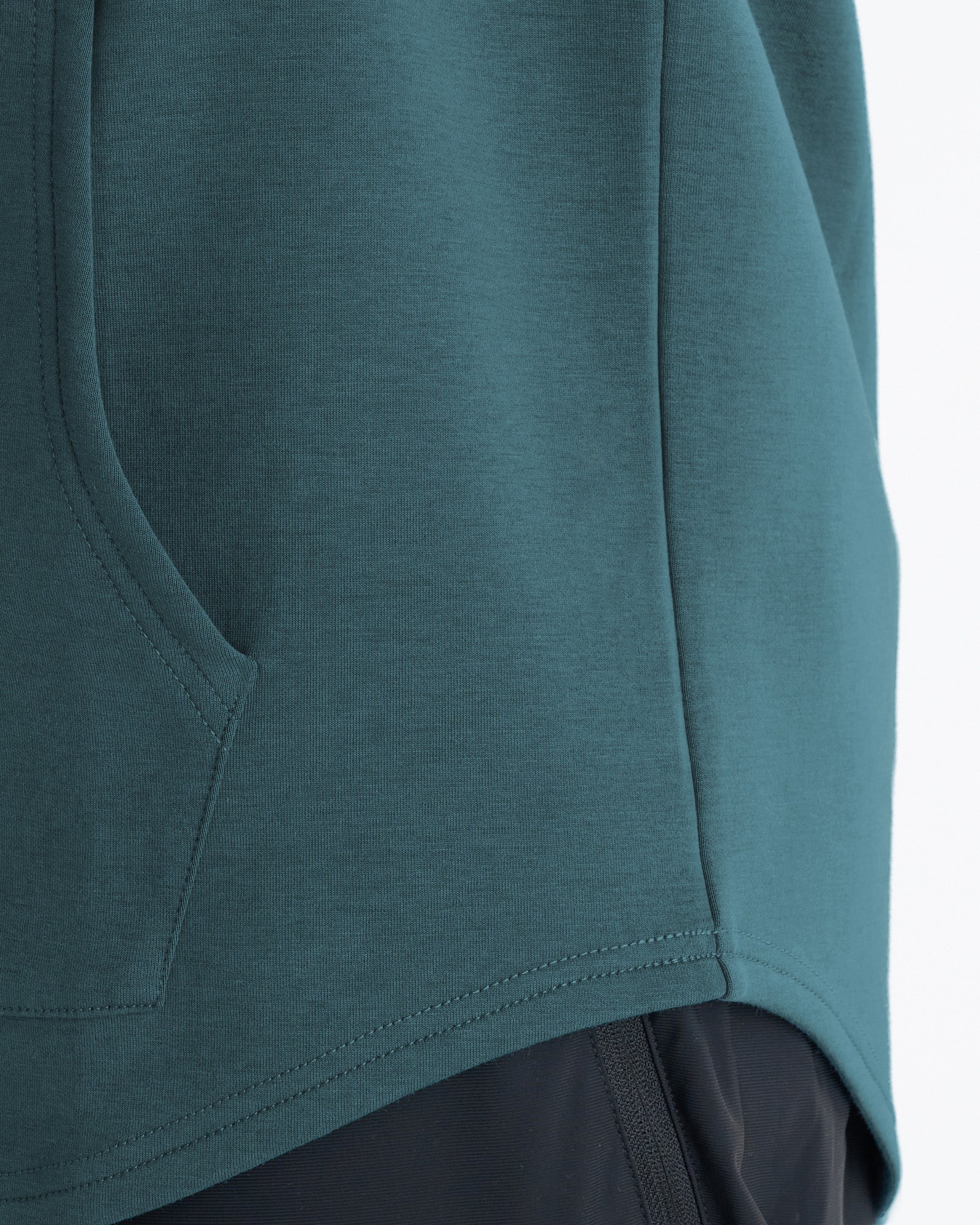 Close-up detail of the Pro-Tech Hoodie in teal showing the kangaroo pocket stitching and curved hem seam.
