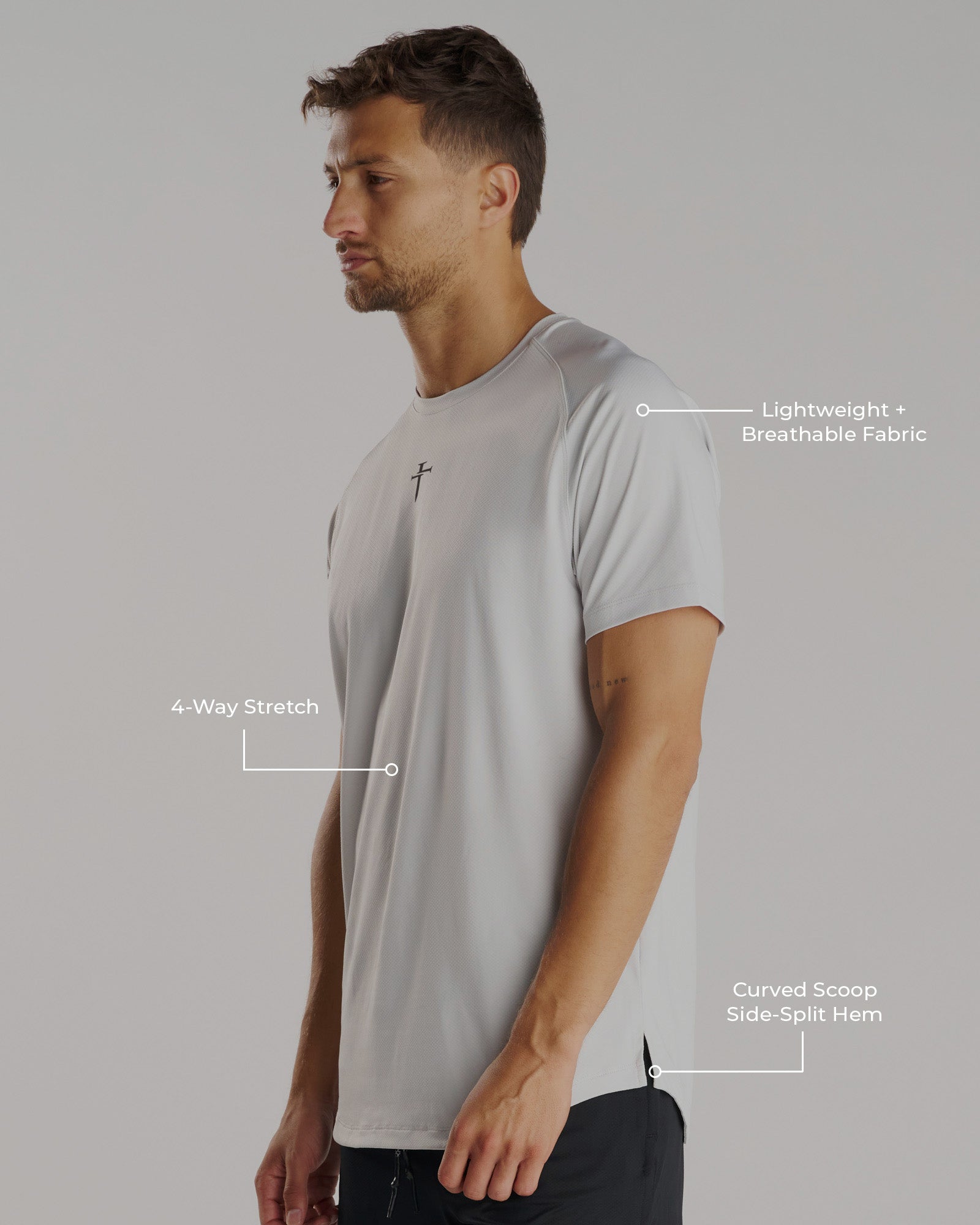 Man wearing the Pro-Tech Tee Cross in Stone, shown from a side angle highlighting stretch fabric and curved hem.