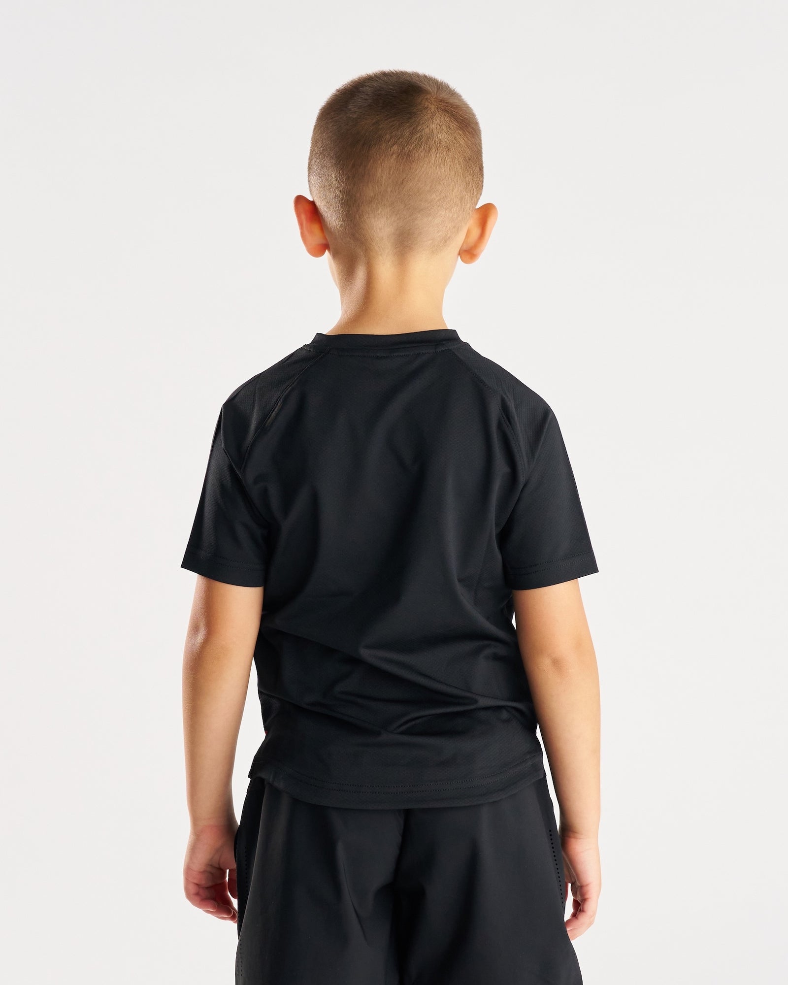 Youth Pro-Tech Tee Cross in black, back view on young boy model with matching black shorts.