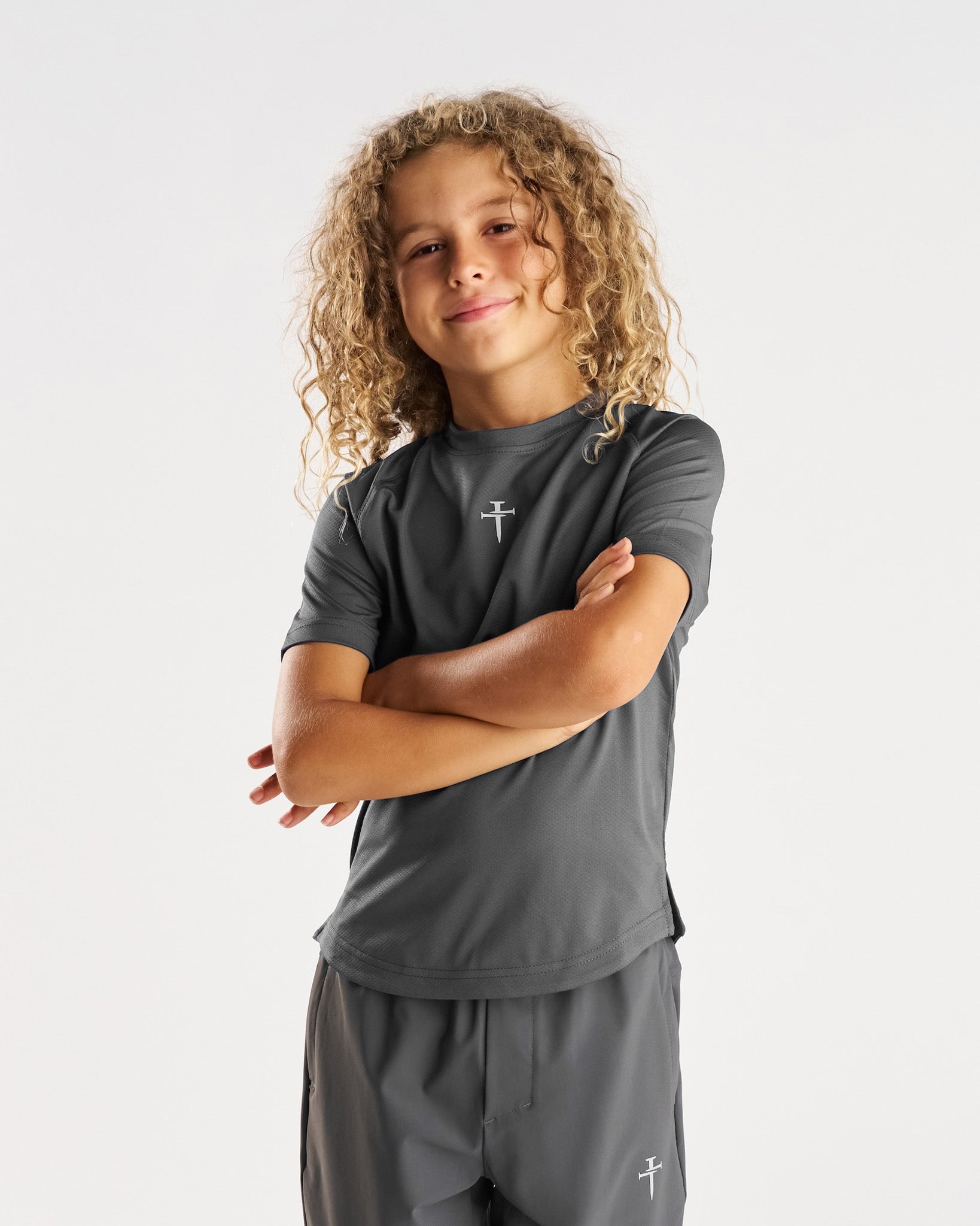 Youth Pro-Tech Tee Cross in Space Grey, front view on young model with arms crossed, matching shorts.