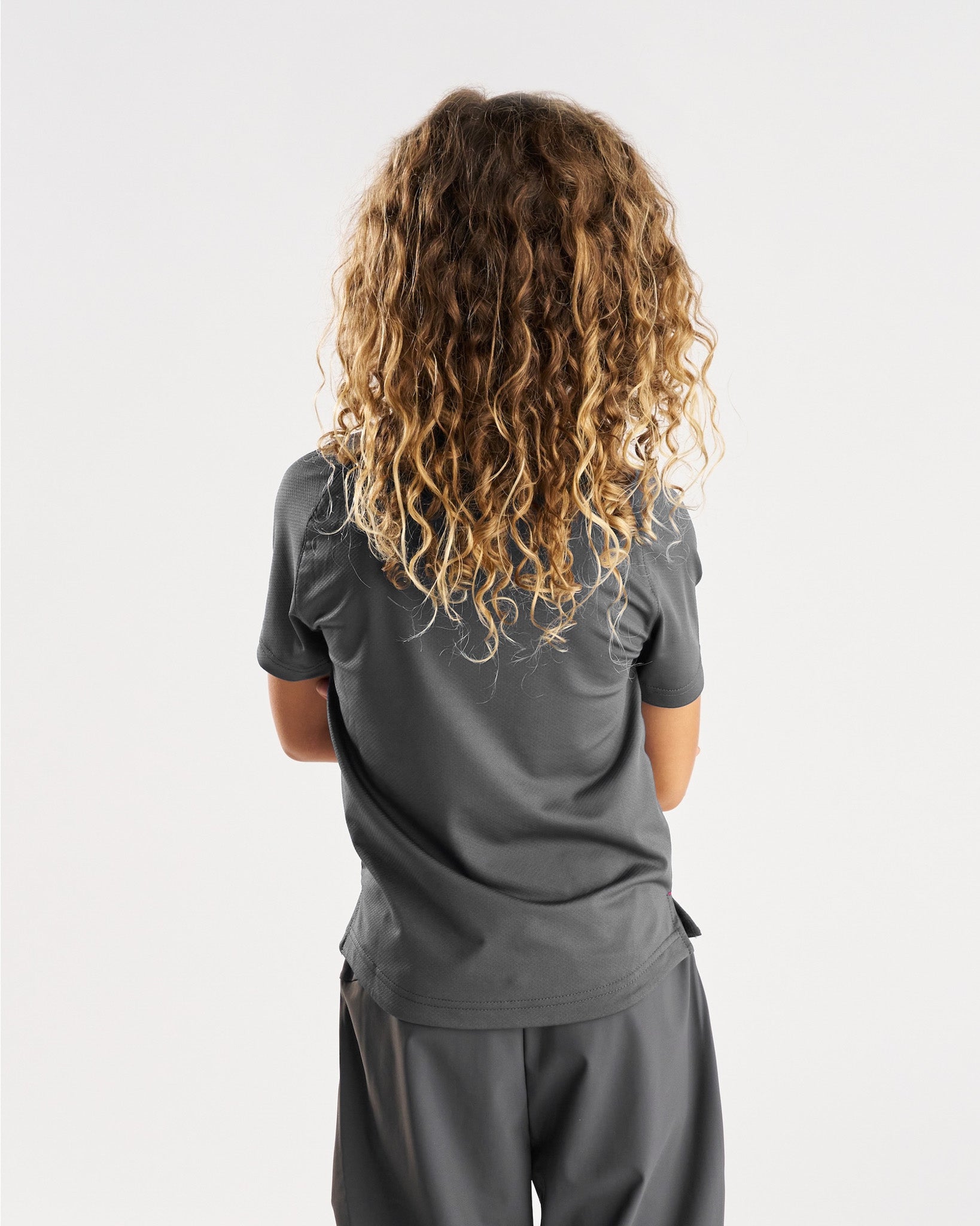 Youth Pro-Tech Tee Cross in Space Grey shown from the back on a model with curly hair.