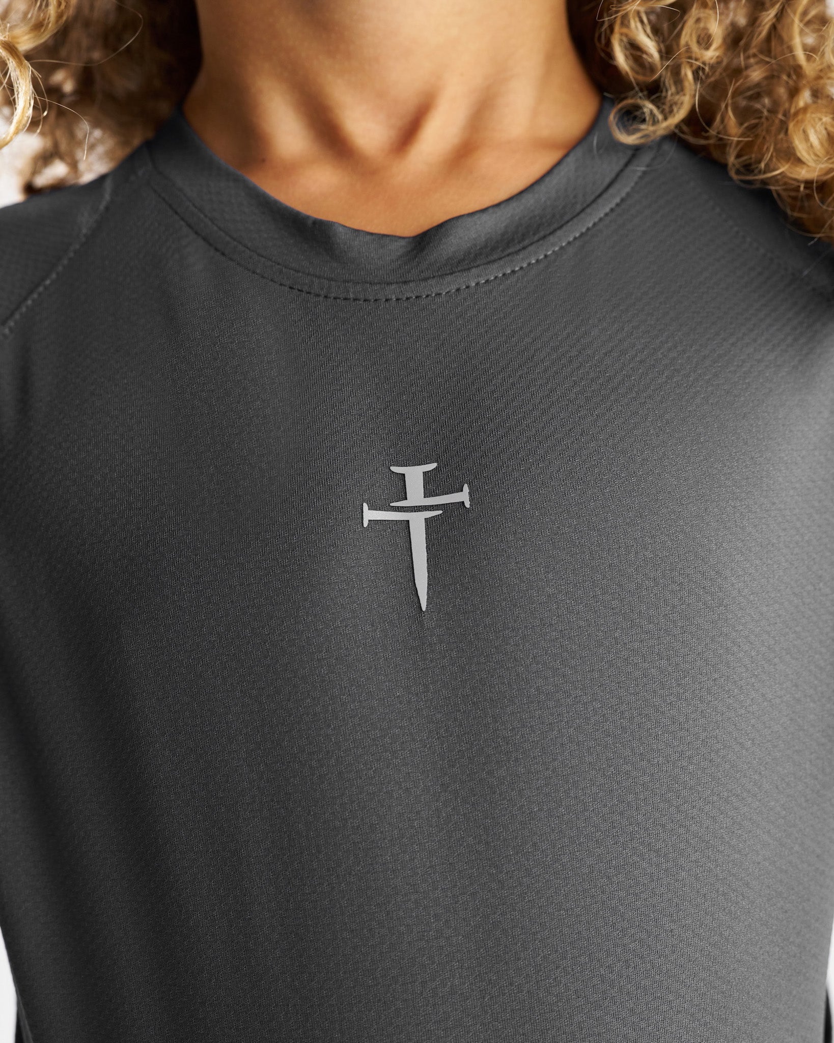 Close-up of the Space Grey Youth Pro-Tech Tee showing the raised nail cross logo on the chest.