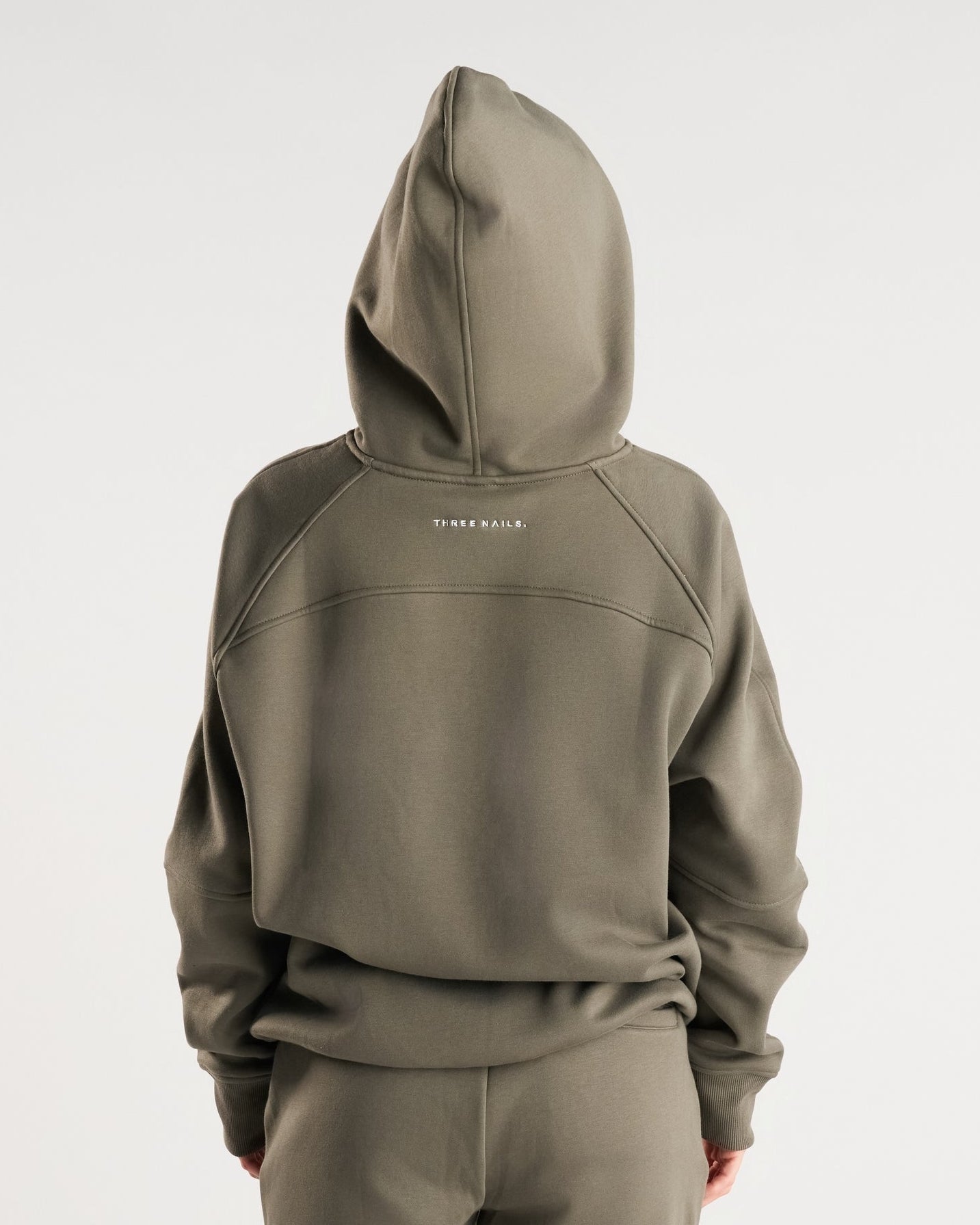Signature Fleece Hoodie in Sage worn by a model, back view, showing hood up and THREE NAILS. logo text.
