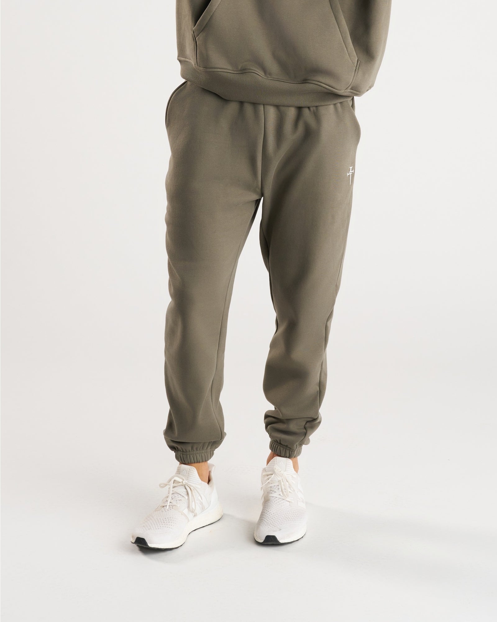 Front view of Signature Fleece Sweatpants in Sage worn with white sneakers, showing relaxed fit and small cross logo.
