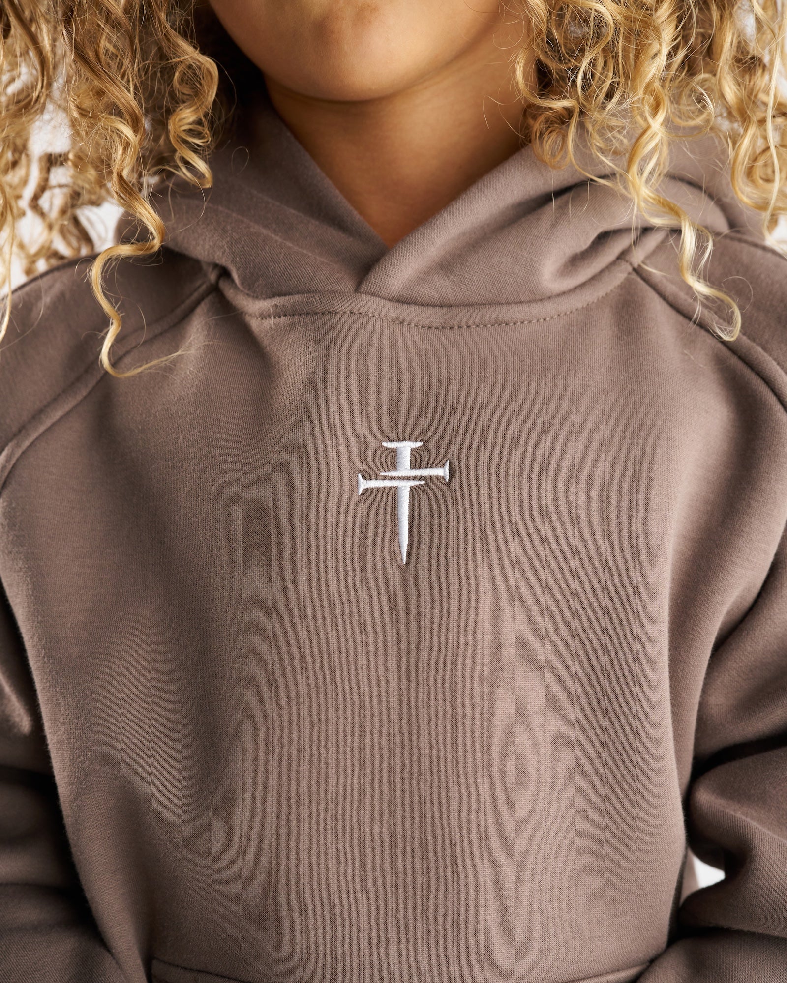 Close-up front view of Youth Signature Fleece Hoodie in Deep Taupe showing embroidered nail cross logo on chest.