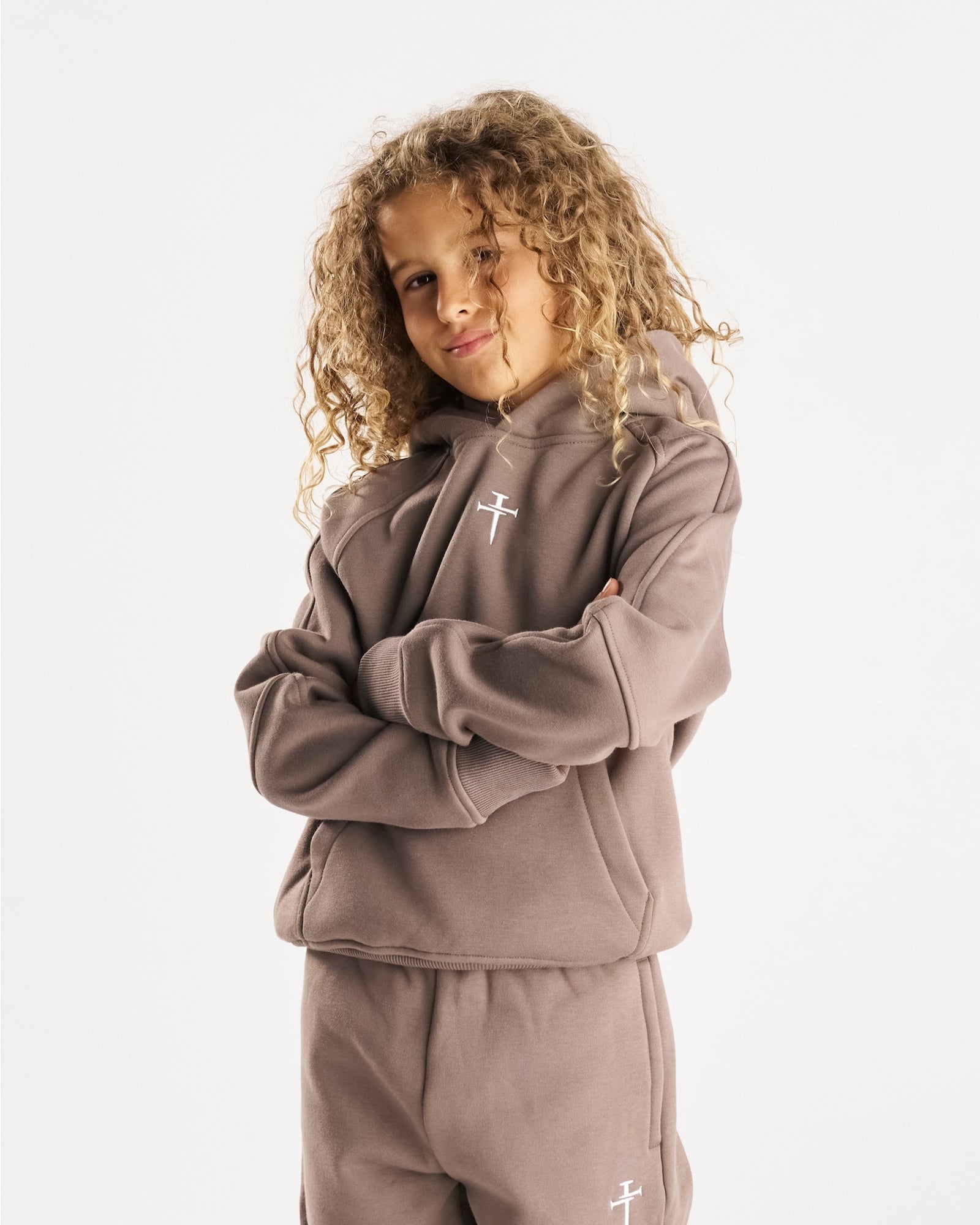 Youth Signature Fleece Hoodie in Deep Taupe on a young model with curly hair, arms crossed, slight front angle.