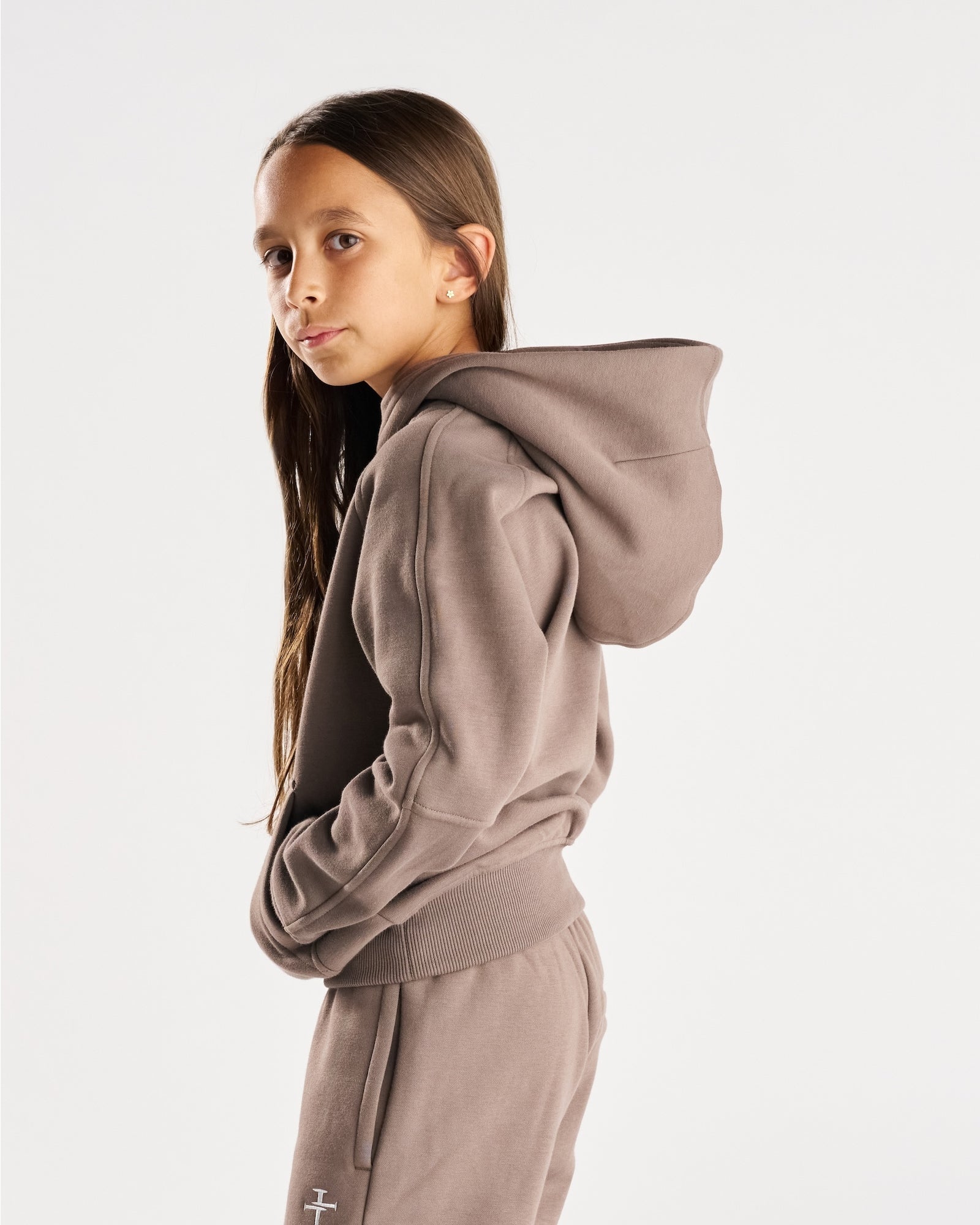 Youth Signature Fleece Hoodie in Deep Taupe shown on a young model from a side angle, looking back toward camera.