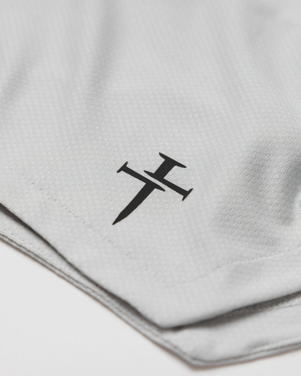 Close-up of the Three Nails logo printed on the Pro-Tech 2.0 Linerless Short in Stone.