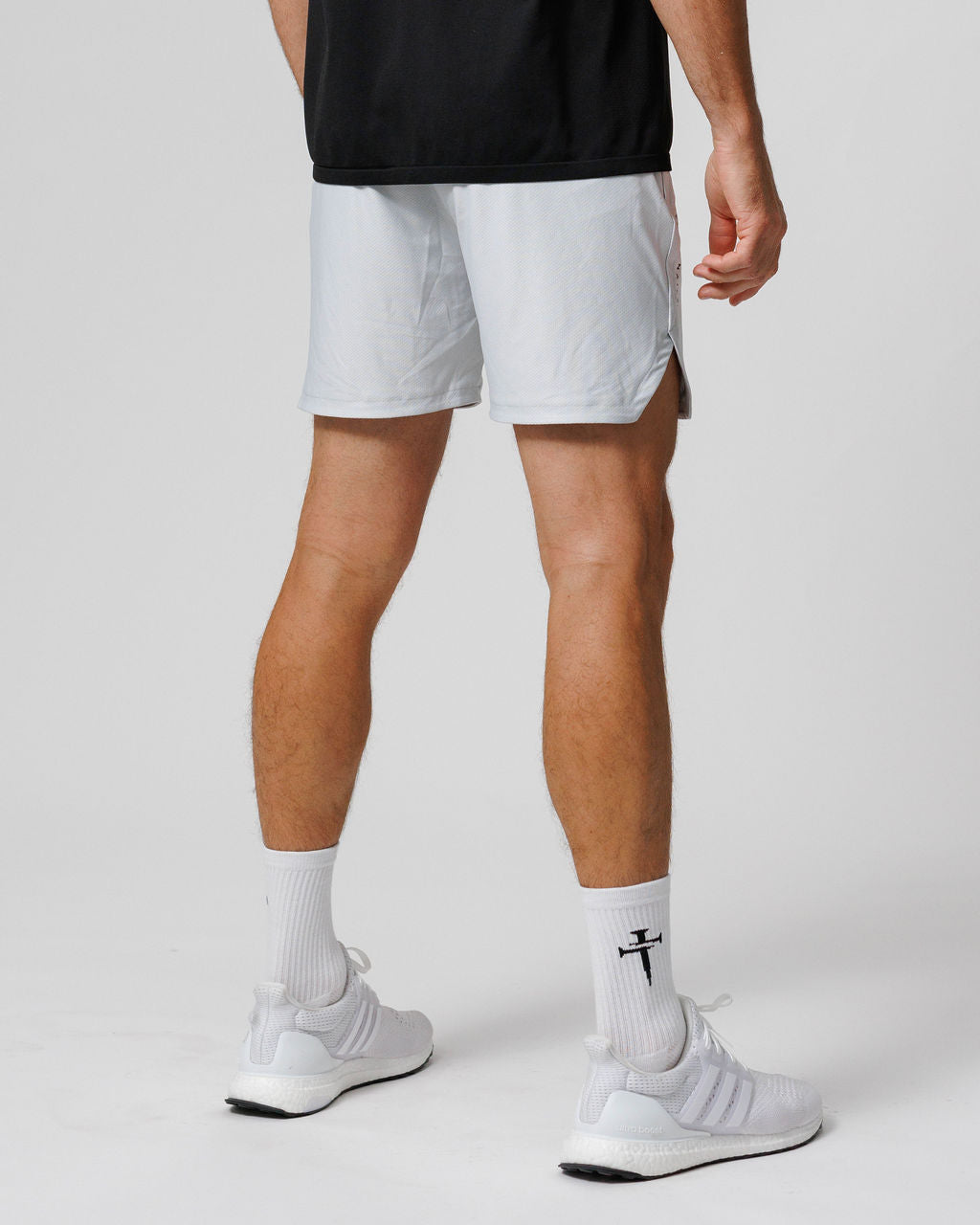 Man wearing Pro-Tech 2.0 Linerless Short in Stone, back angle view, paired with white Adidas sneakers and crew socks.