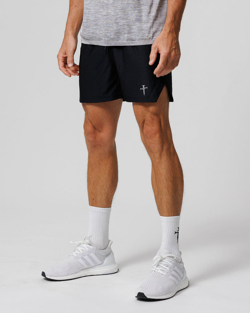 Man wearing black Pro-Tech 2.0 Linerless Shorts, front angle, paired with white Adidas sneakers and branded socks.
