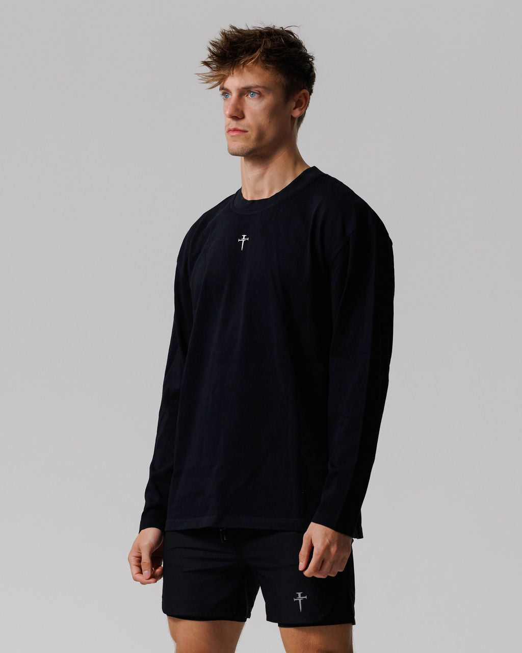 Male model wearing black Heavyweight Cotton Oversized Long Sleeve at a side angle, paired with matching black shorts.