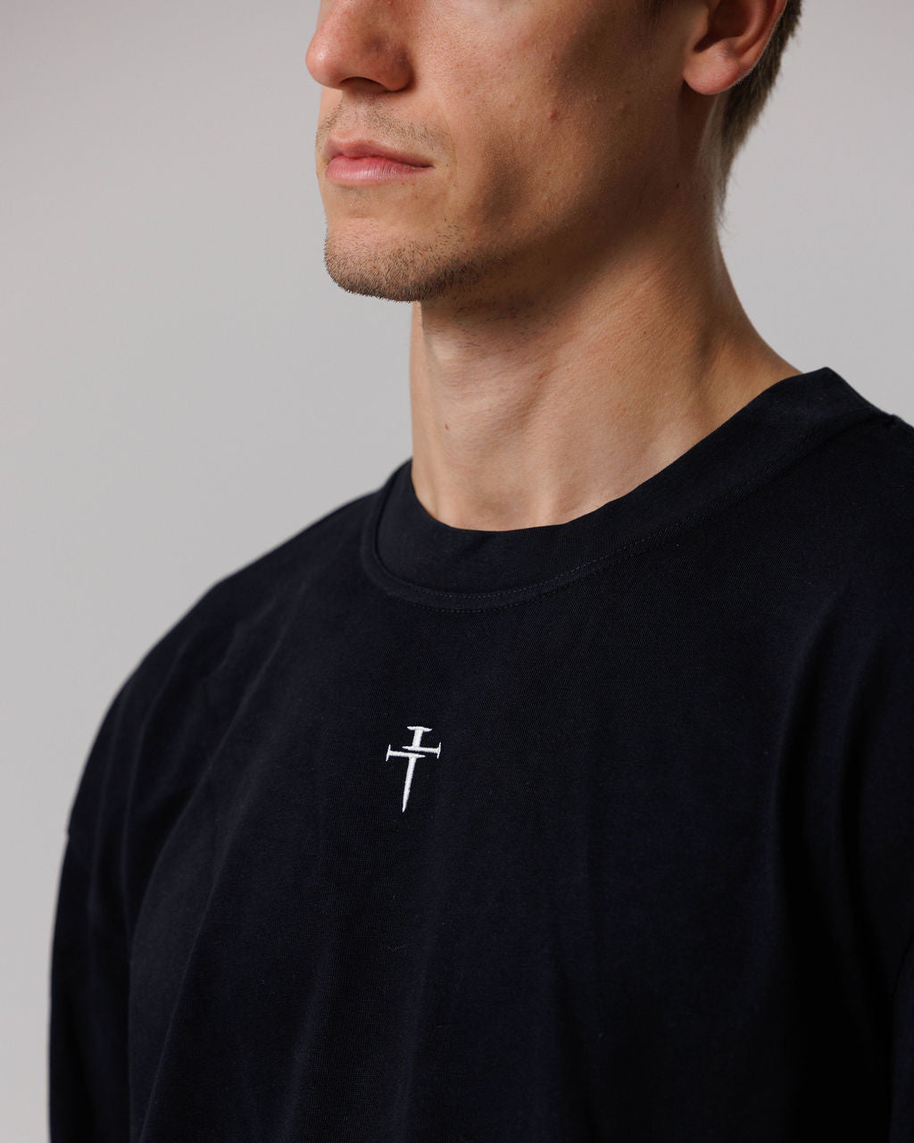Close-up of black Heavyweight Cotton Oversized Long Sleeve on male model showing embroidered nail cross detail on chest.