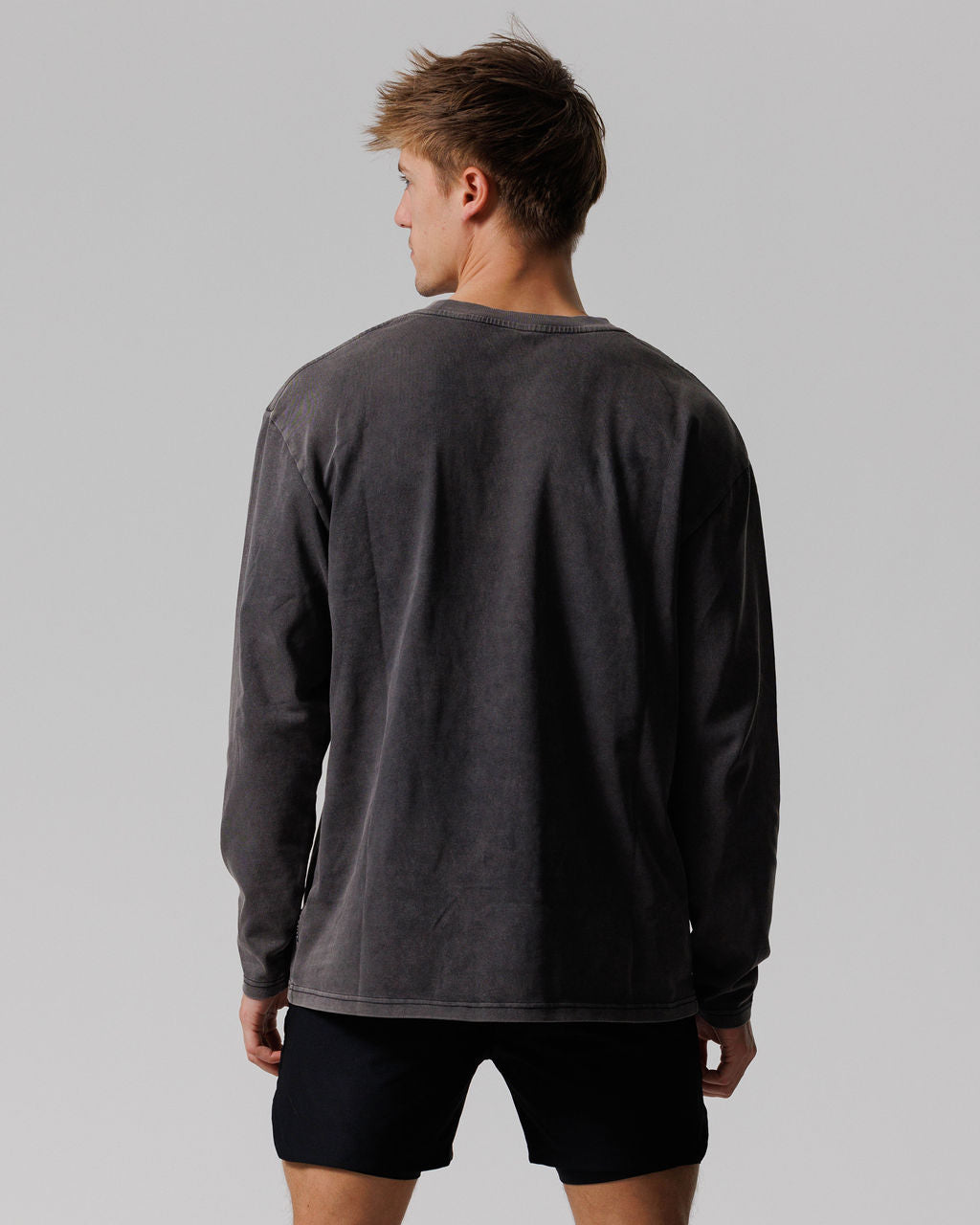 Back view of model wearing the Heavyweight Cotton Oversized Long Sleeve in Acid Wash charcoal paired with black shorts.