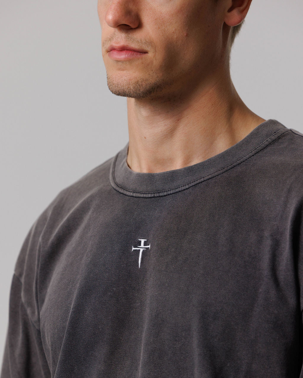 Close-up of Heavyweight Cotton Oversized Long Sleeve in Acid Wash, showing embroidered nail cross logo on chest.
