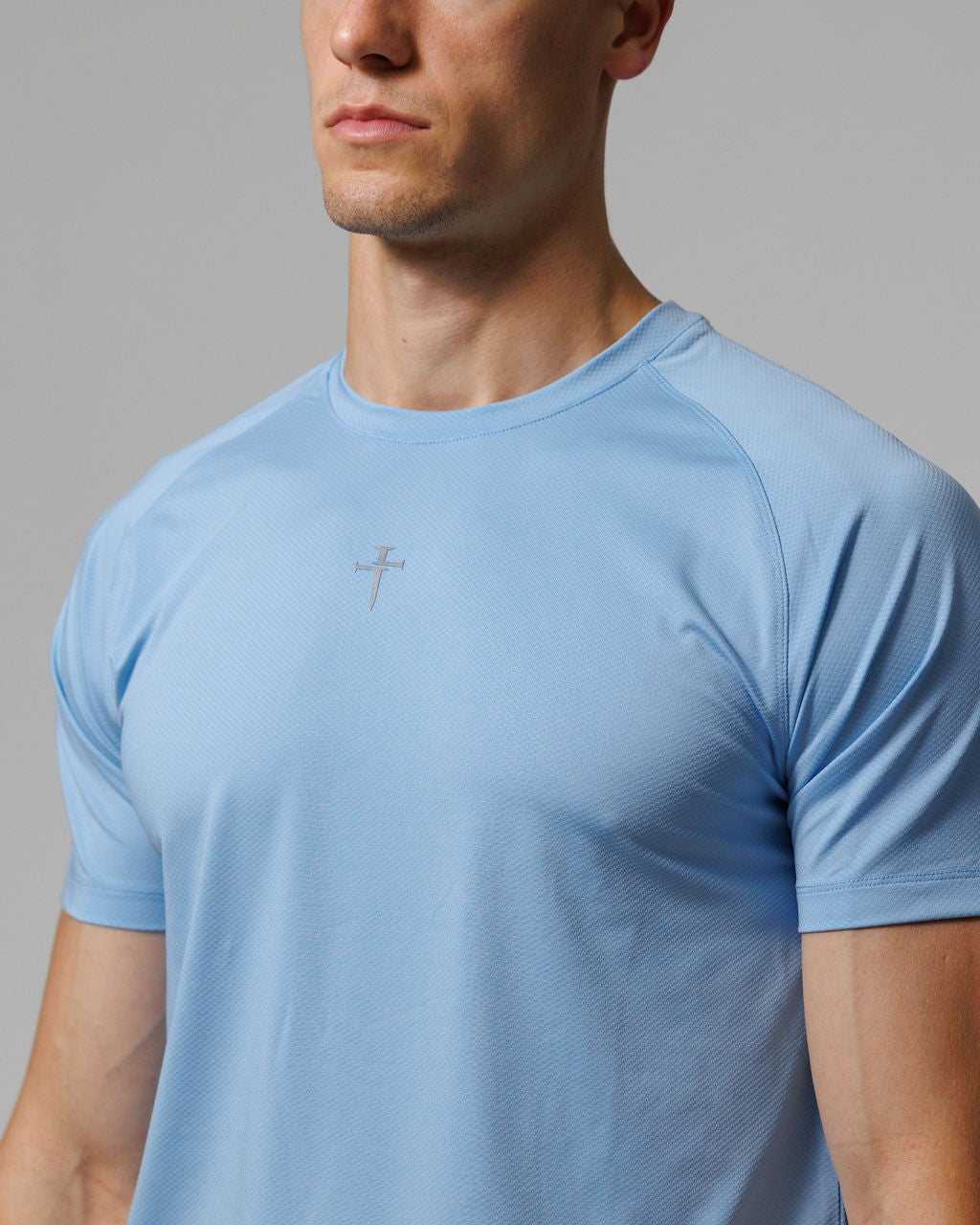 Male model wearing sky blue Pro-Tech Tee Cross, front angle close-up highlighting subtle cross logo on chest.