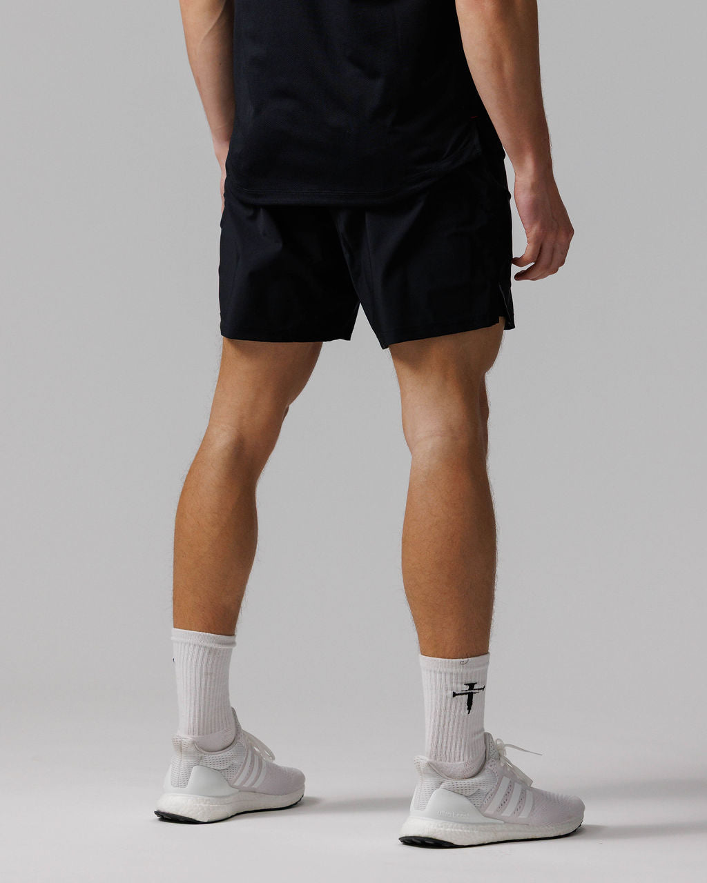 Man wearing black Vapor-Lite Hybrid Shorts, back view, paired with white sneakers and socks.