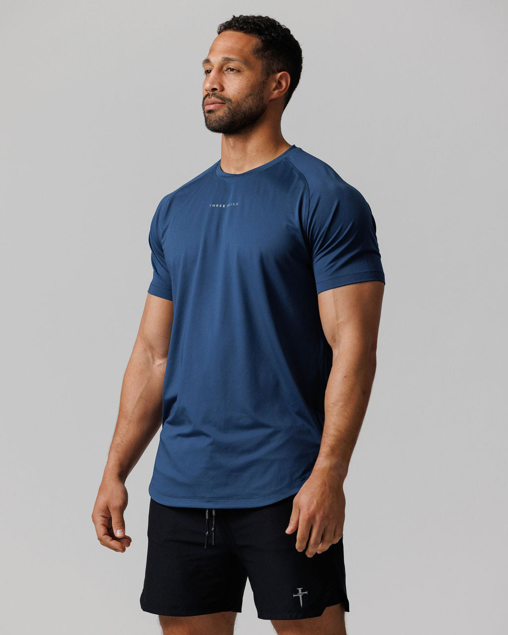 Pro-Tech Tee Three Nails in Midnight Navy worn by a male model at a slight side angle, paired with black shorts.