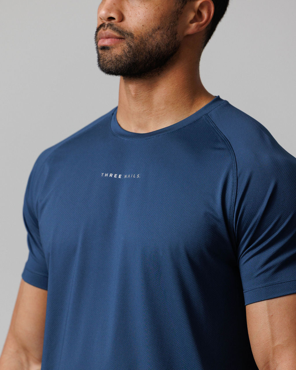 Close-up front view of Pro-Tech Tee Midnight Navy showing chest logo, raglan sleeves, and textured fabric detail.