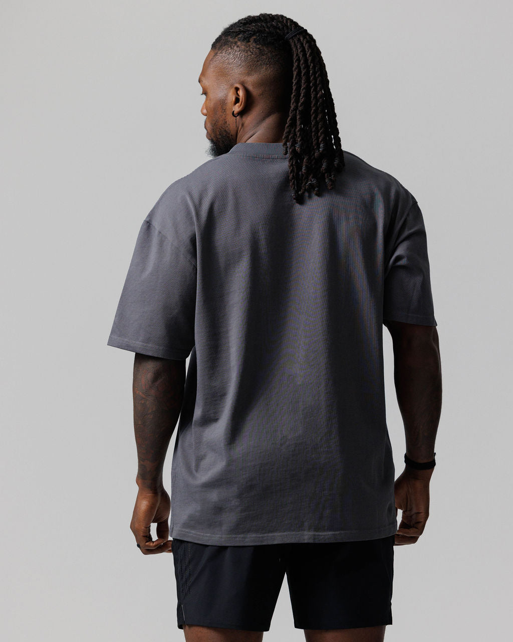 Back view of model wearing the Heavyweight Cotton Oversized Tee in Space Grey Cross with black shorts.