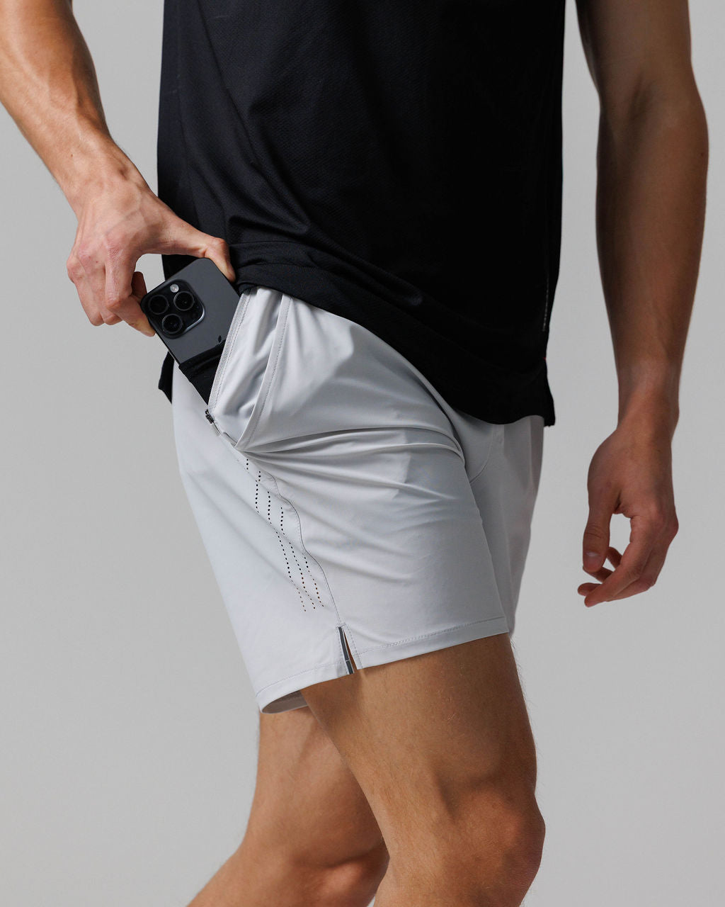 Side angle view of Vapor-Lite Hybrid Short in Stone with model pulling phone from zippered side pocket.