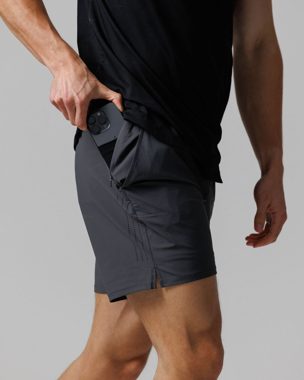 Side angle view of Vapor-Lite Hybrid Short in Space Grey, model inserting phone into zippered side pocket.